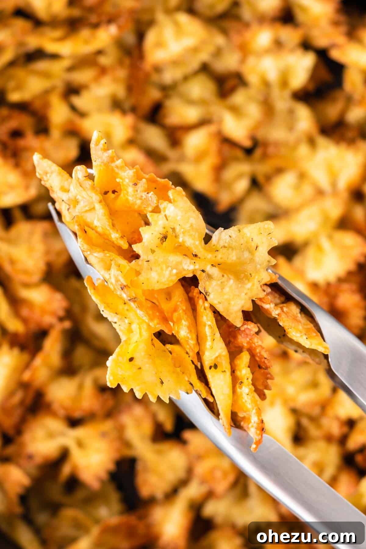 Tongs picking up crispy pasta chips from the air fryer basket