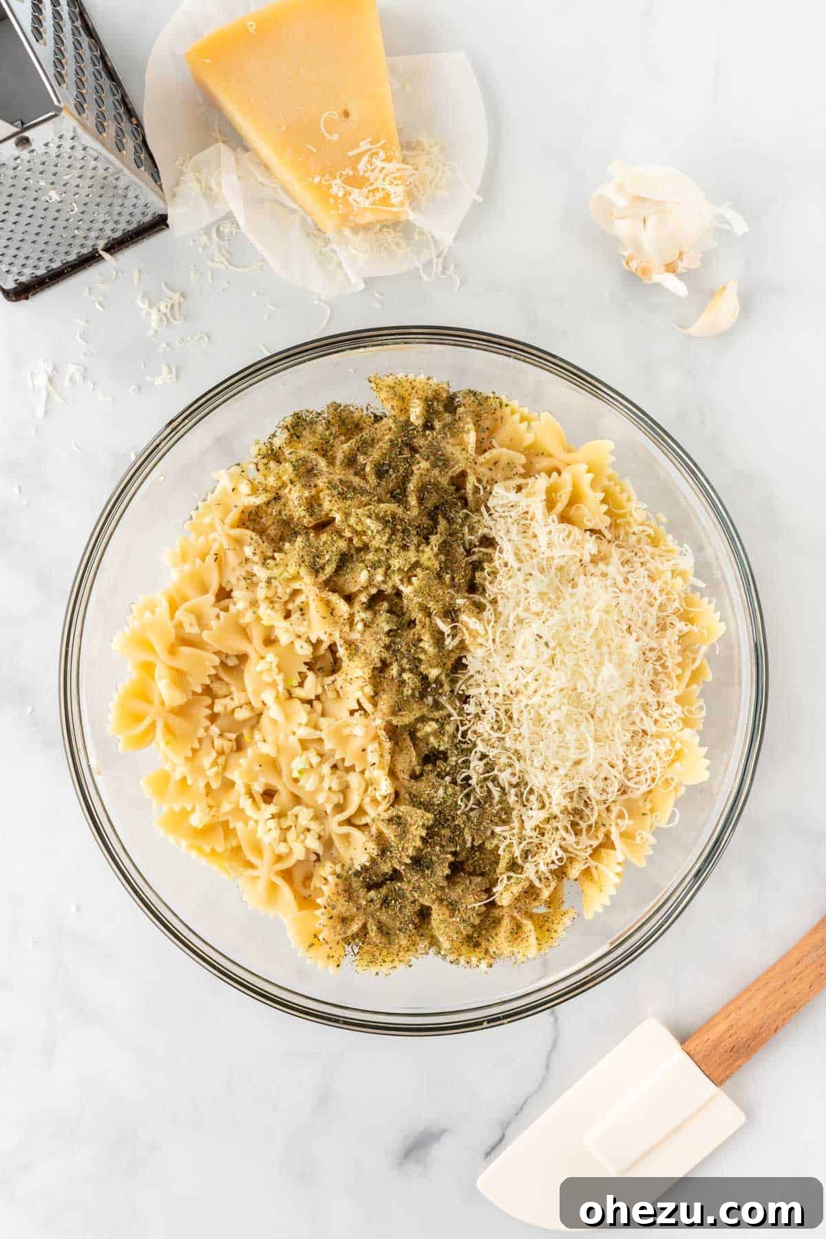 Adding spices and parmesan cheese to cooked pasta in a mixing bowl