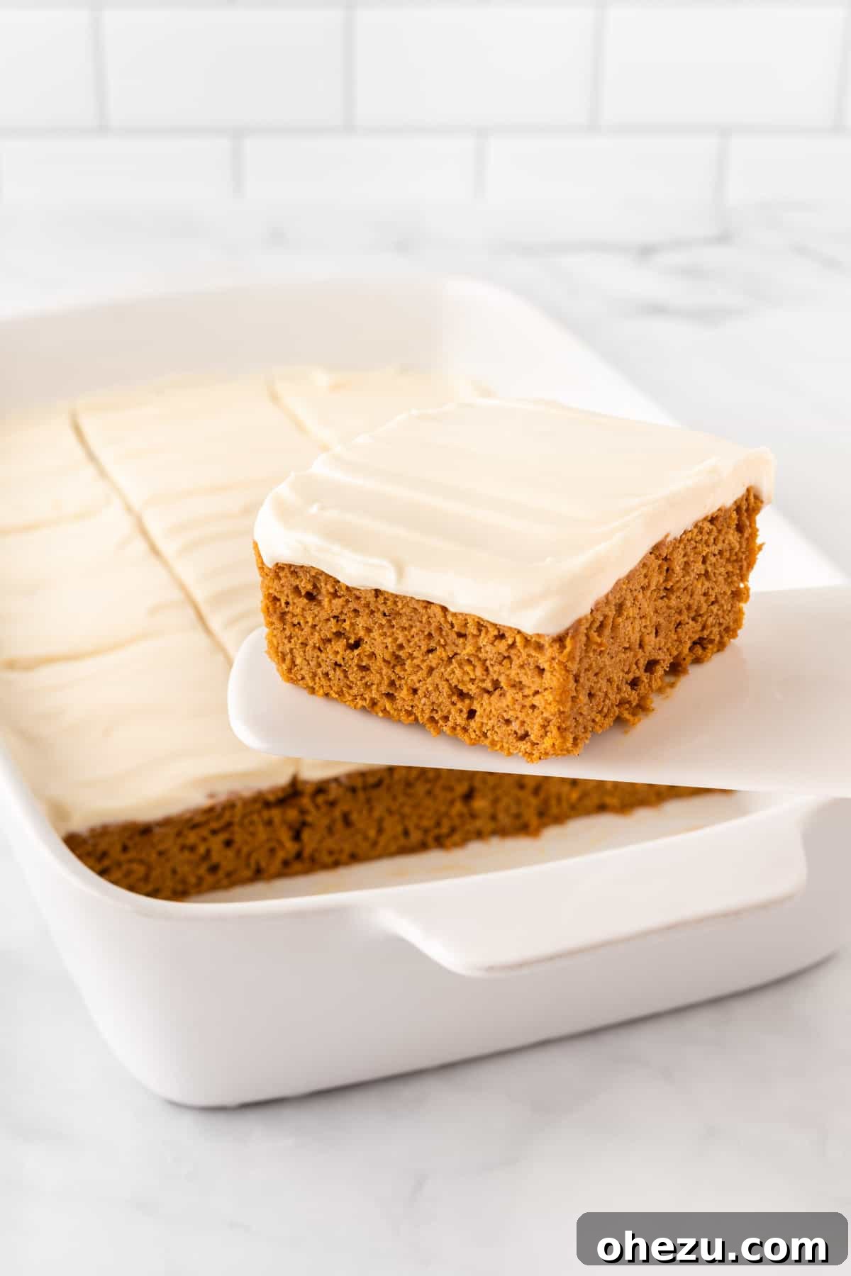 Effortless Fall Spiced Pumpkin Bars 2 A slice of moist cake mix pumpkin bar with rich cream cheese frosting being lifted from a baking pan, showcasing its perfect texture and inviting golden-brown crust.