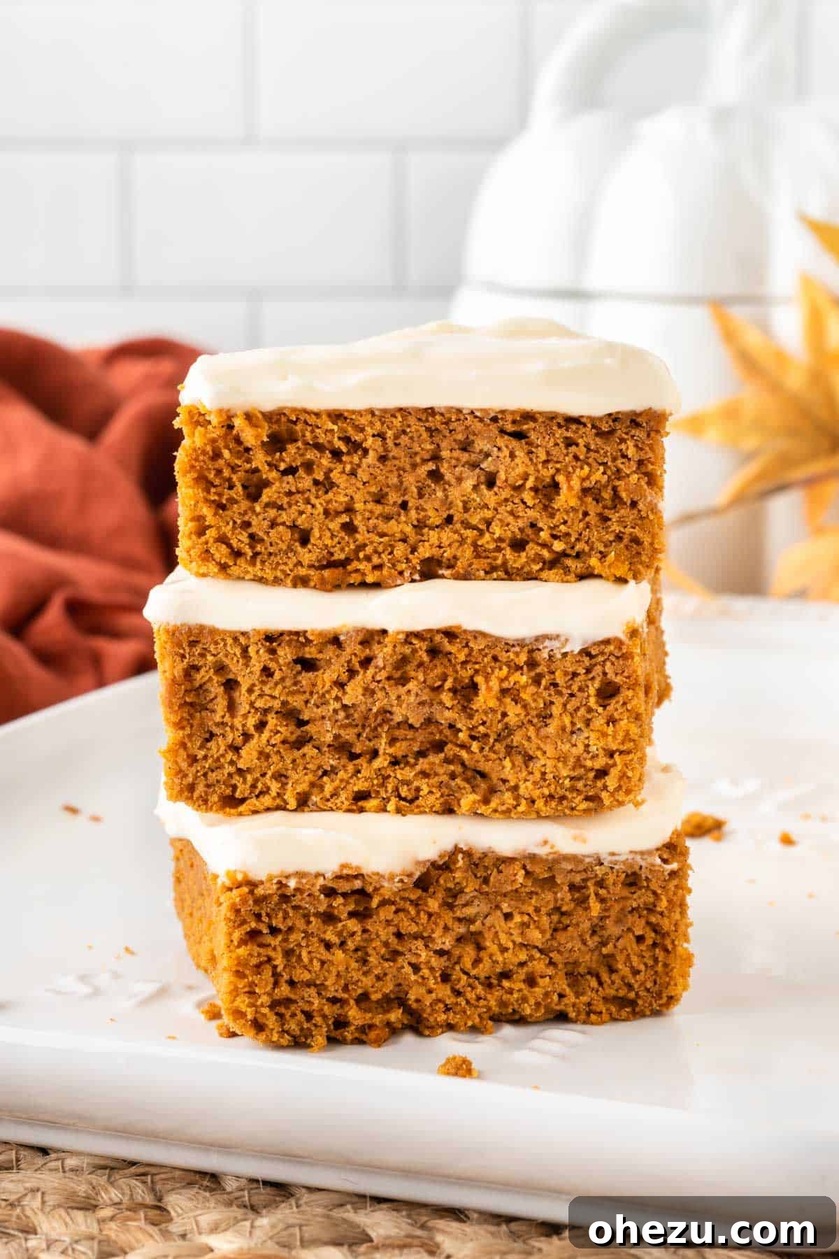 Effortless Fall Spiced Pumpkin Bars 12 Three individual cake mix pumpkin bars, generously frosted with cream cheese frosting, stacked neatly on top of each other, highlighting their height and delicious layers.