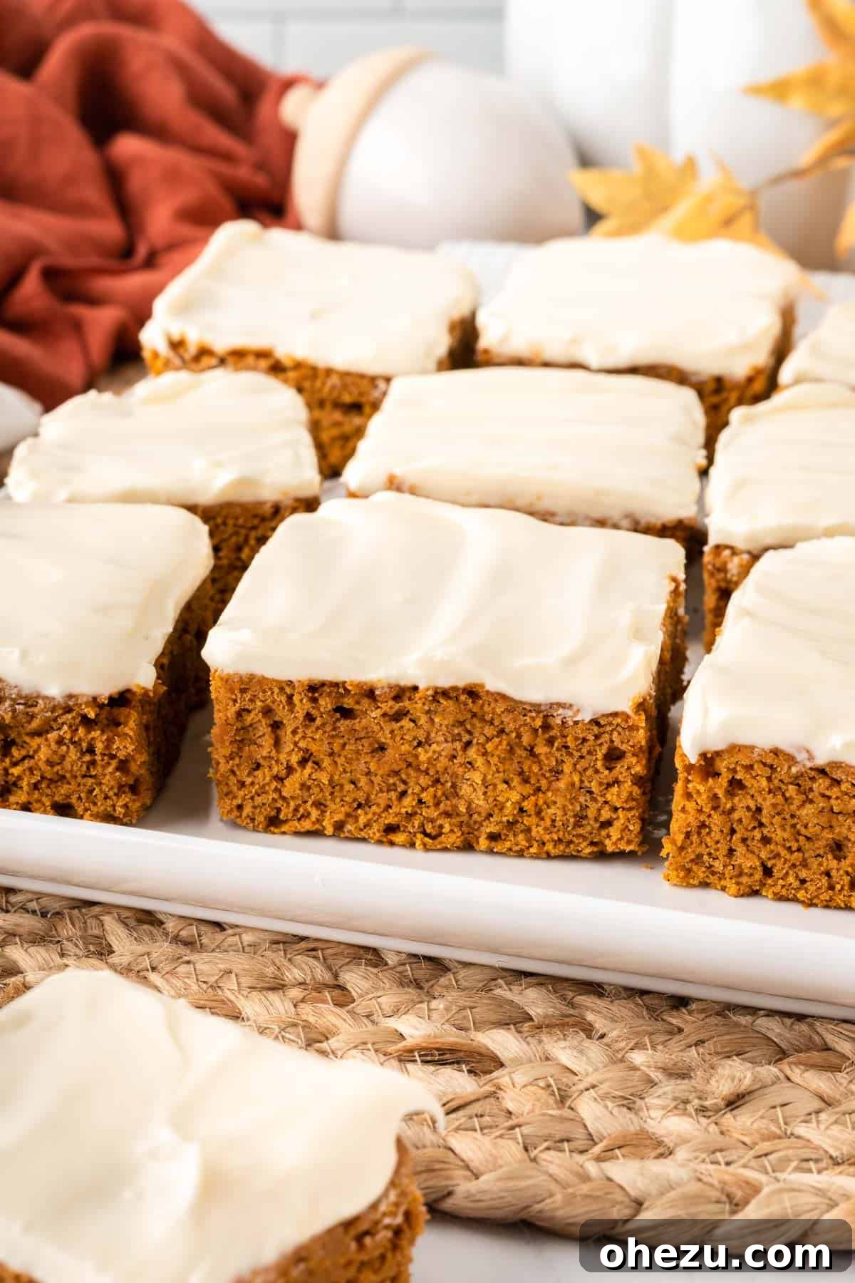 Effortless Fall Spiced Pumpkin Bars 3 Close-up of a single cake mix pumpkin bar, featuring its soft, spiced interior and a thick layer of creamy white cream cheese frosting, sitting on a rustic wooden surface.