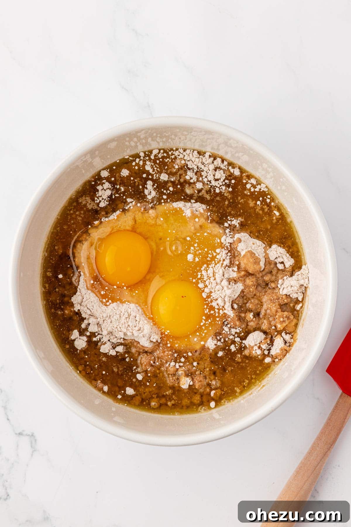 A mixing bowl containing dry spice cake mix, two eggs, and oil, poised for the mixing process.