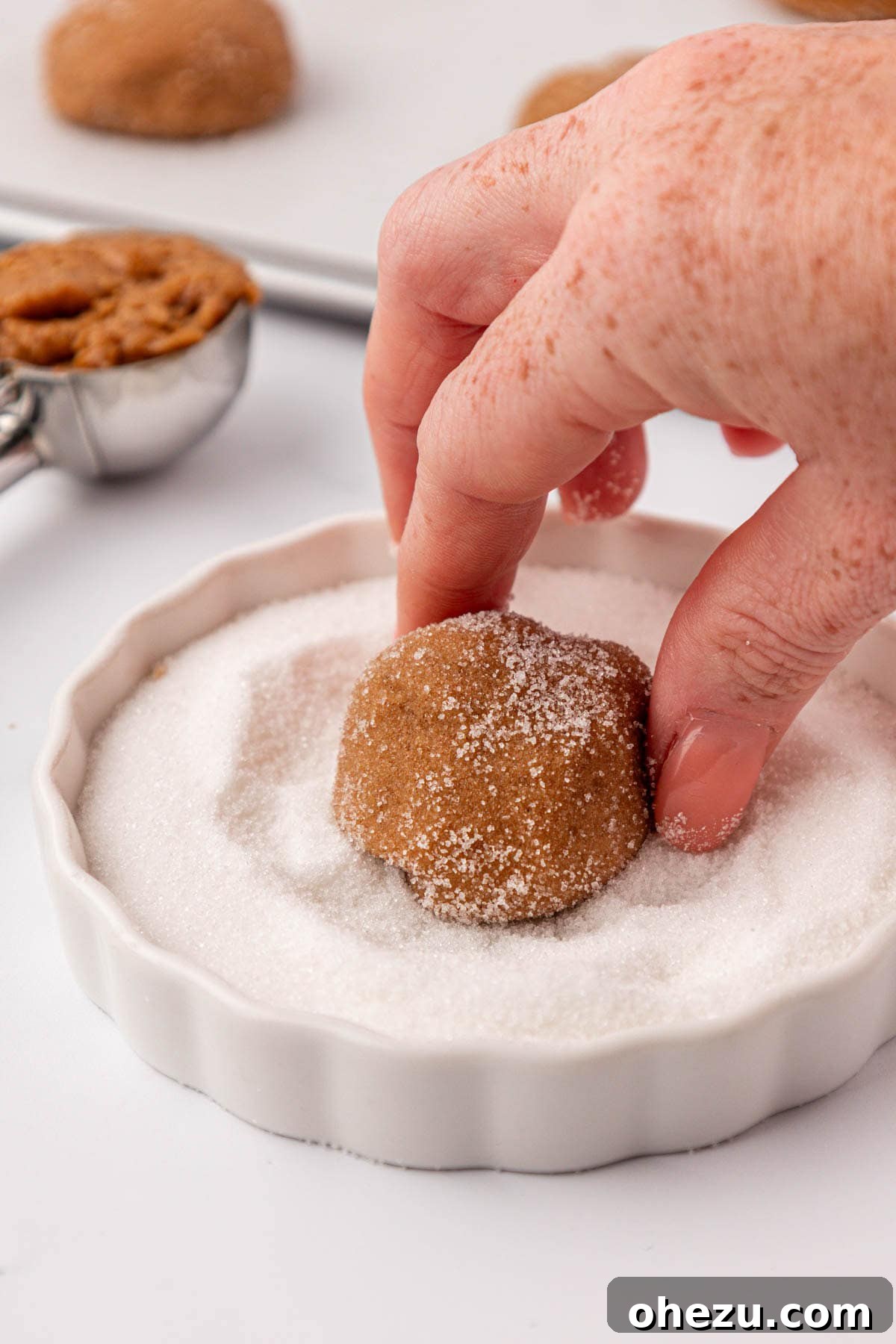 A close-up view of the cookie dough ball being meticulously dipped and coated in sparkling granulated sugar.