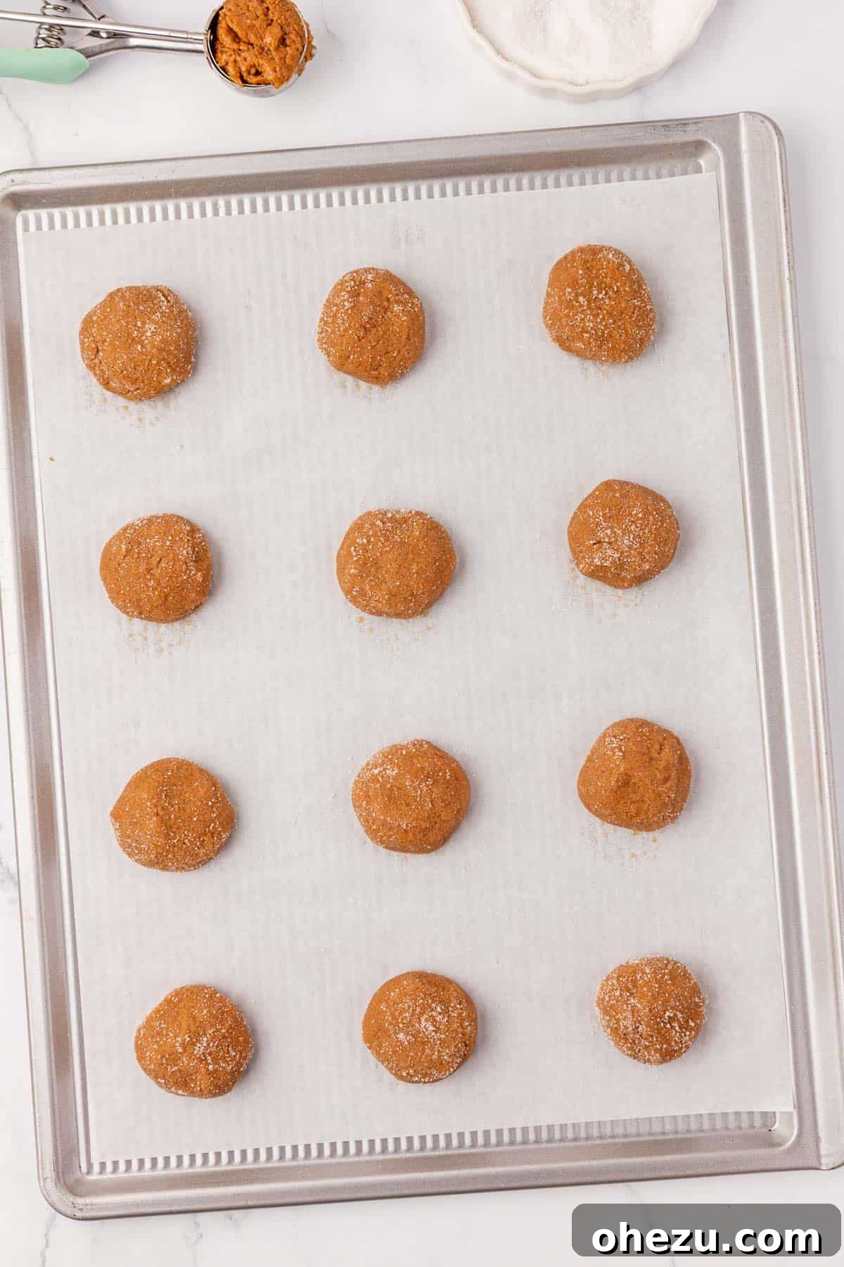 Neatly arranged balls of sugar-coated cookie dough on a baking sheet, ready for the oven.