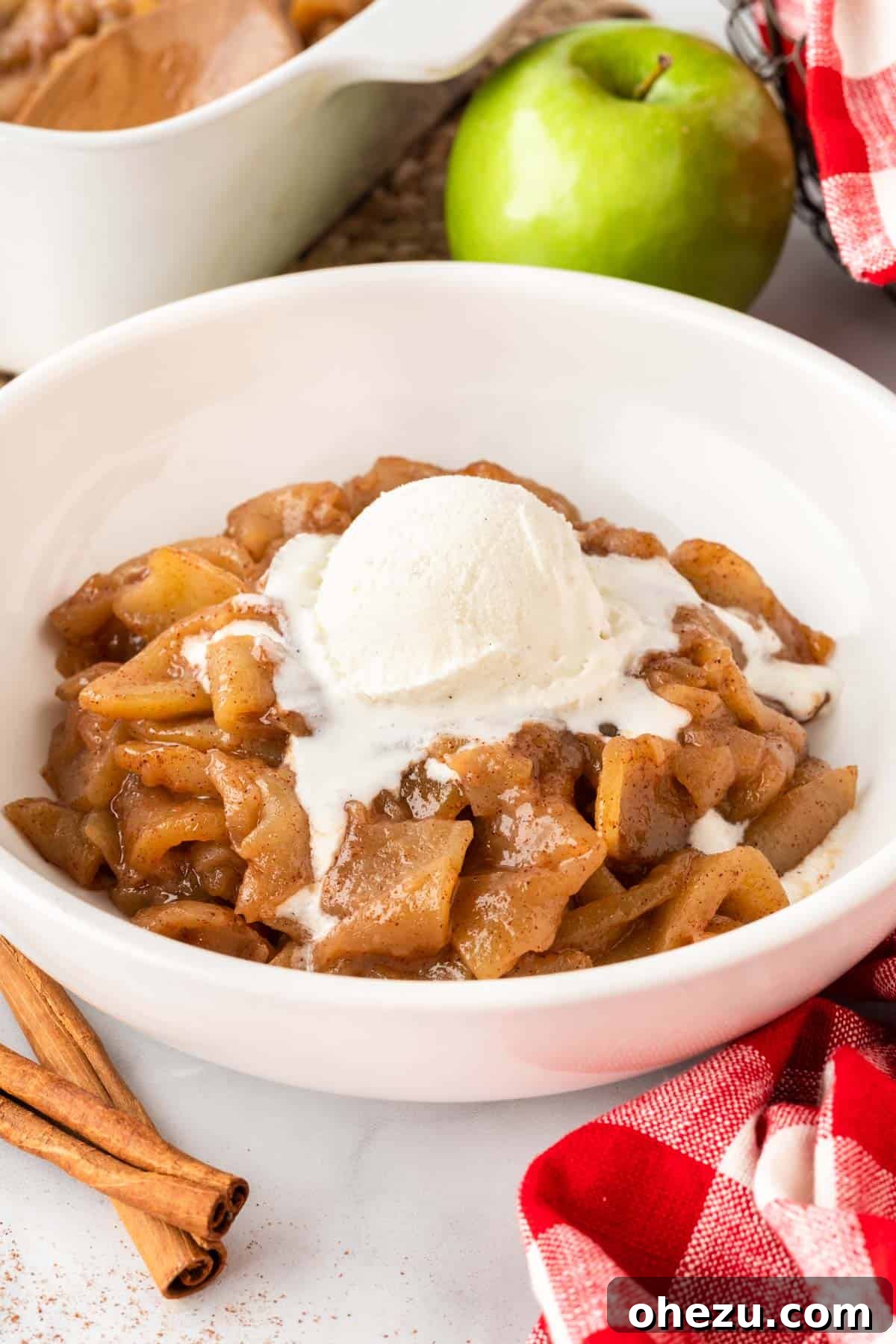 A bowl of warm baked cinnamon apples topped with a generous scoop of melting vanilla ice cream, ready to be enjoyed.