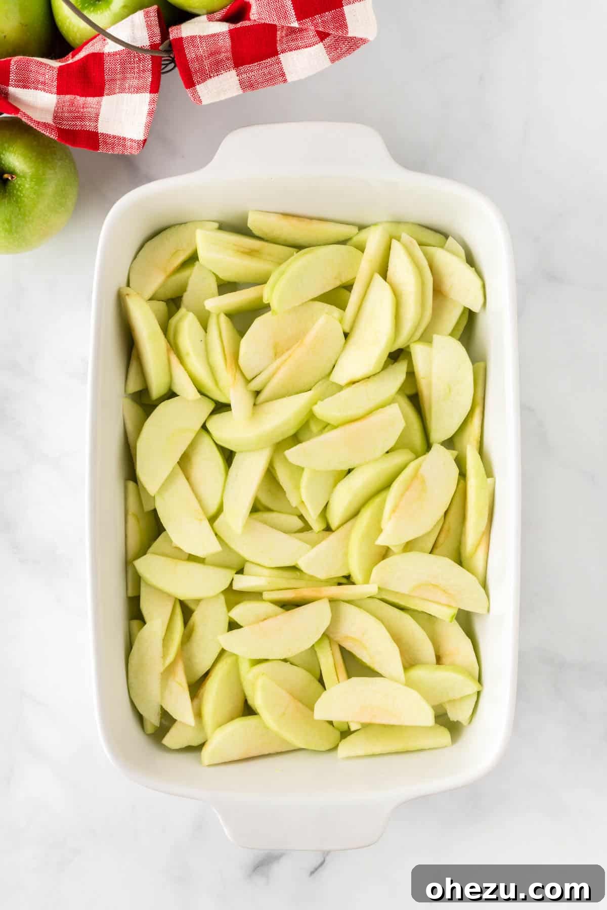 Thinly sliced Granny Smith apples neatly arranged in the bottom of a greased 9x13 inch baking dish, ready for seasoning.
