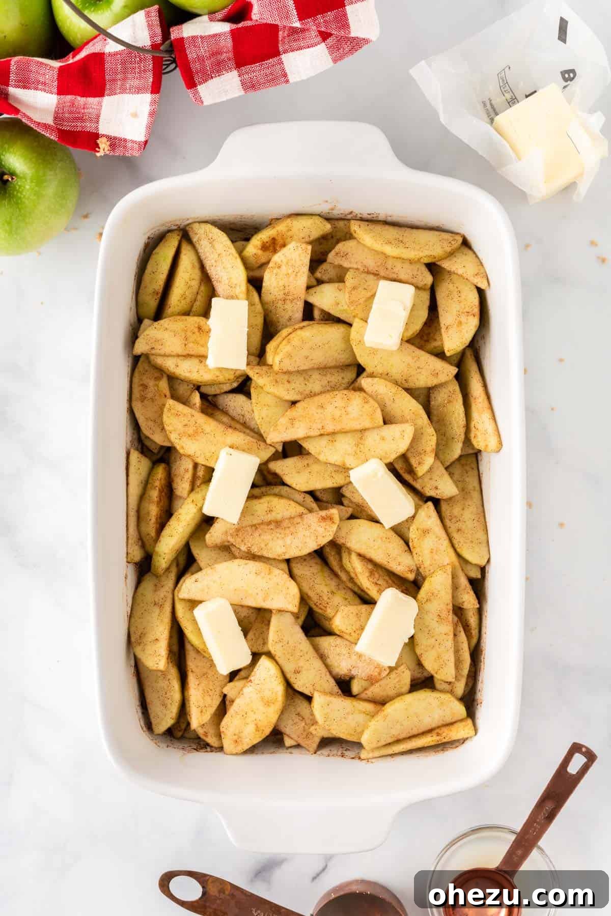 Small cubes of butter carefully placed over the spiced apple slices in the baking dish, anticipating a rich, melted sauce.