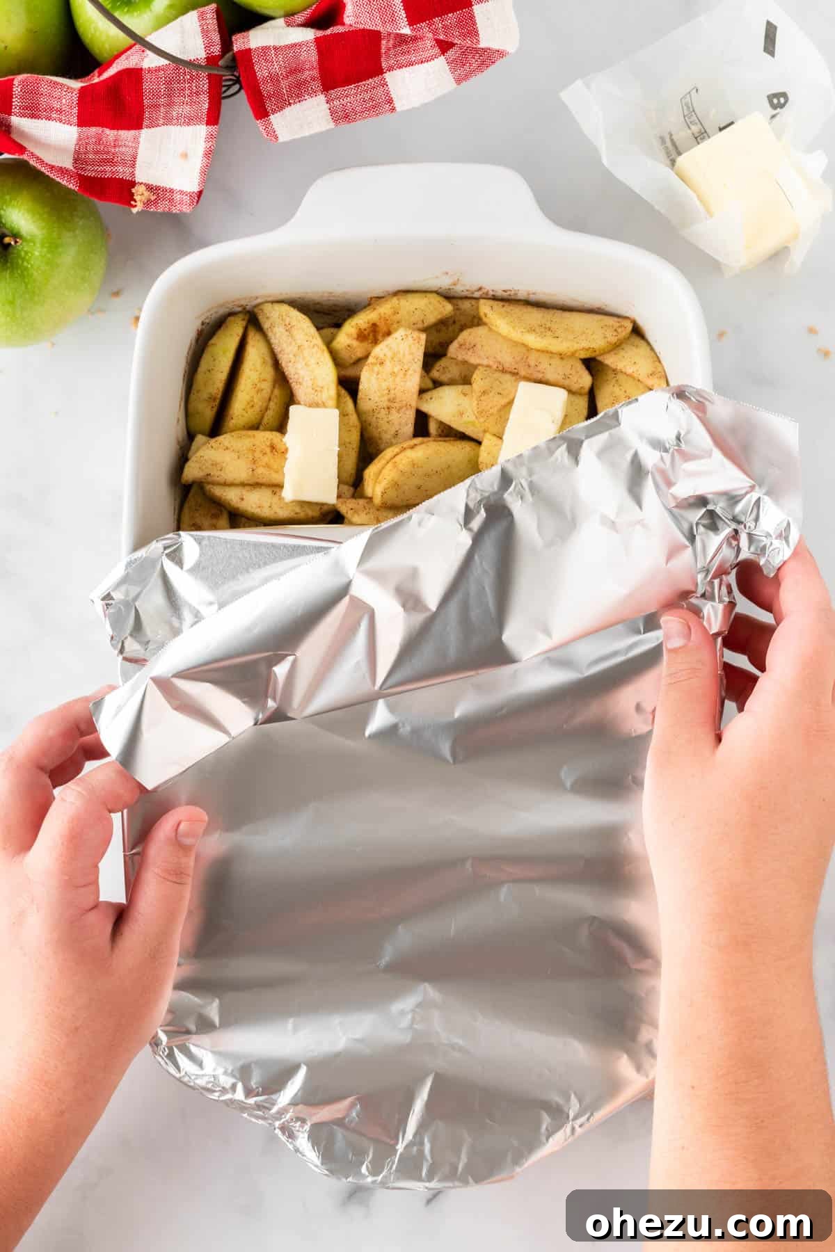The baking dish filled with seasoned apples and butter, securely covered with aluminum foil, ready to go into the oven for its first phase of baking.