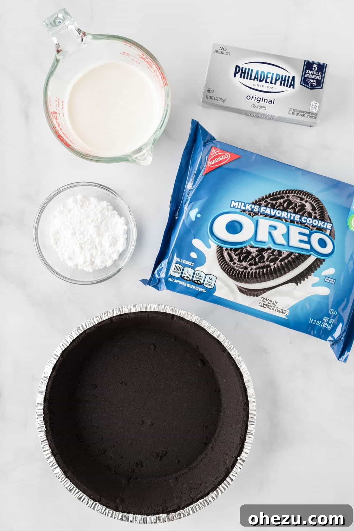 Decadent Oreo Delight 4 A flat lay photograph showcasing the simple ingredients needed for No-Bake Oreo Pie: heavy cream, powdered sugar, cream cheese, and a stack of Oreo cookies next to a pre-made Oreo pie crust.