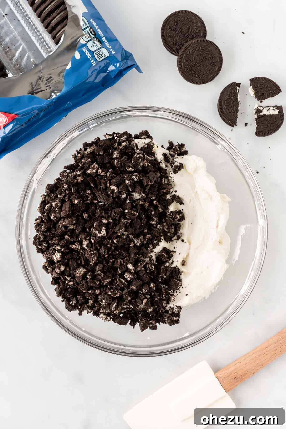 Decadent Oreo Delight 6 A rubber spatula gently folding crushed Oreo cookies into the rich, white cream cheese and whipped cream filling in a mixing bowl.