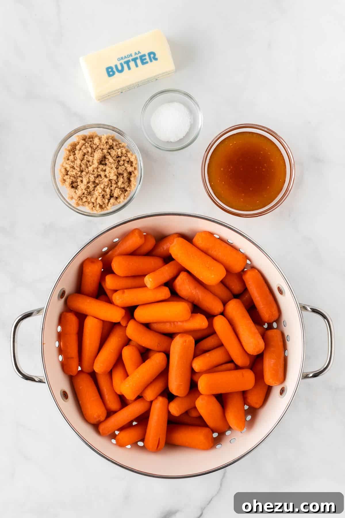 A flat lay photograph of the simple ingredients needed: a bag of baby carrots, a stick of butter, a bowl of brown sugar, and a jar of honey.