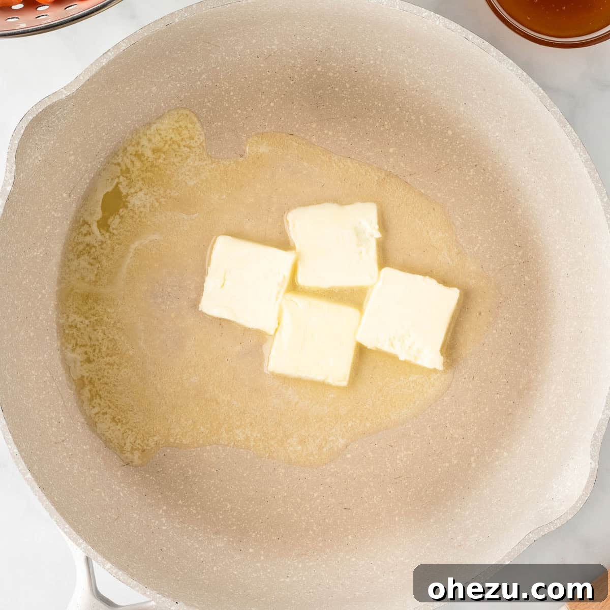 A block of butter melting and bubbling in a hot skillet, ready for the carrots.