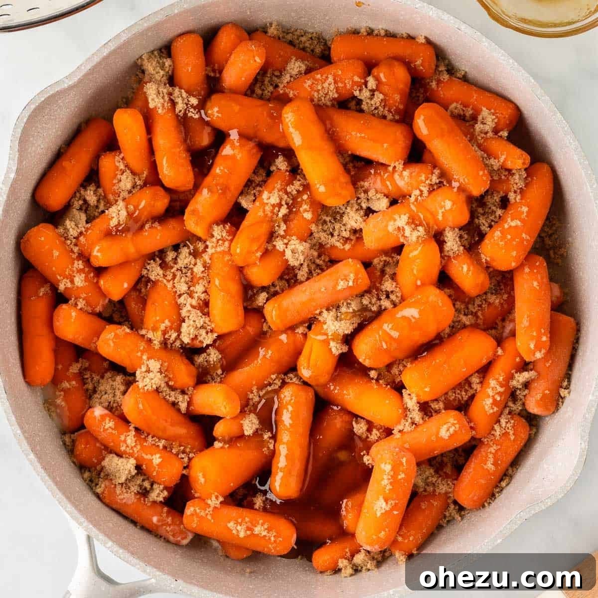 Baby carrots, topped with a generous layer of brown sugar, in a skillet with melted butter.