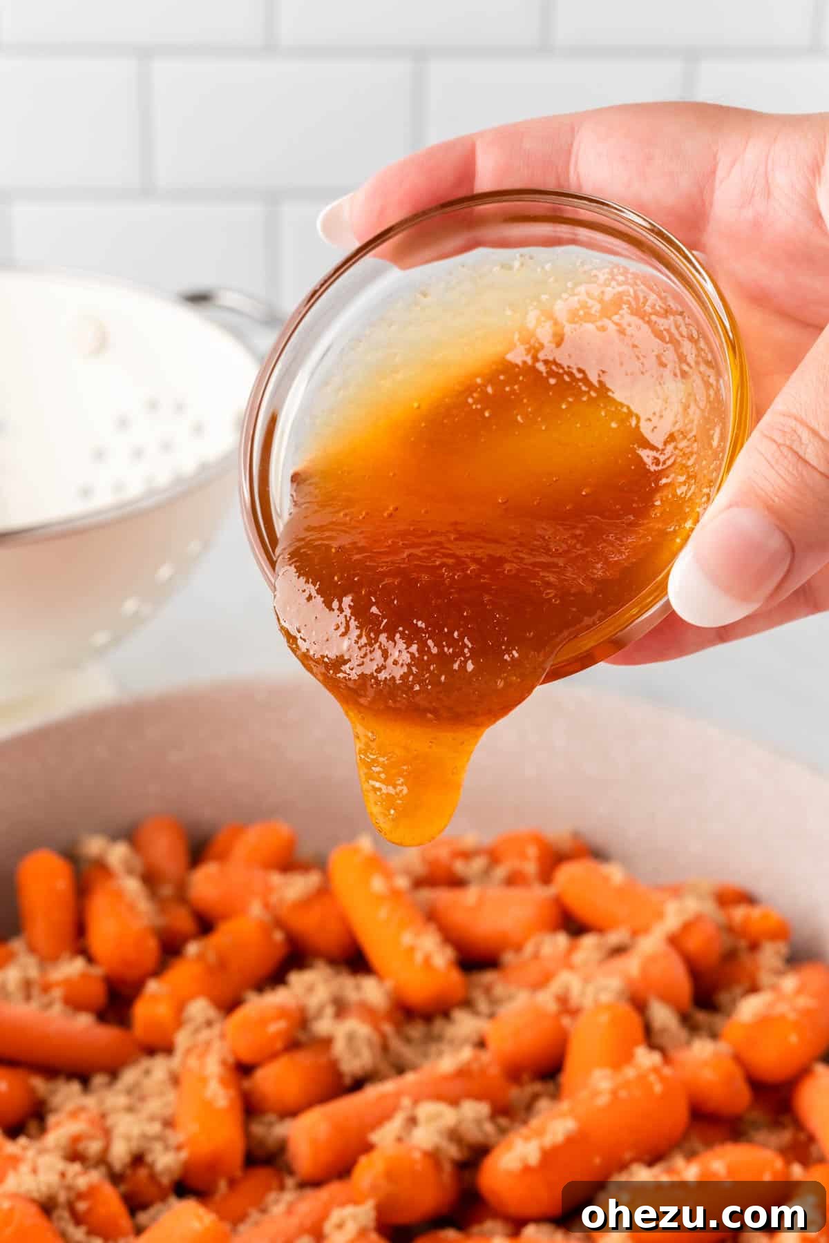 A stream of golden honey being poured over baby carrots and brown sugar in a hot skillet, preparing for the glaze to form.