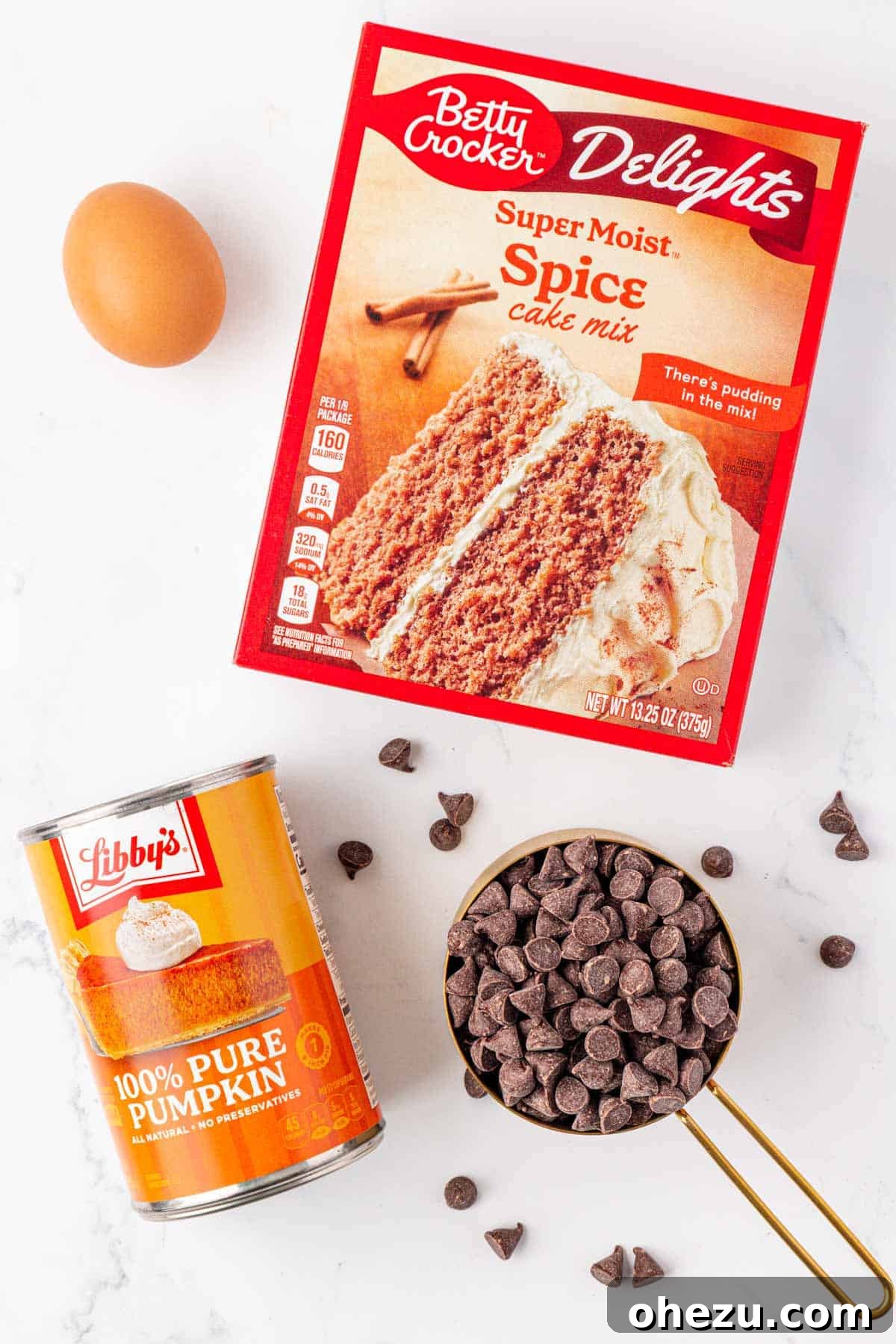 Individual ingredients laid out: a large egg, a box of spice cake mix, a bag of chocolate chips, and a can of pumpkin puree.