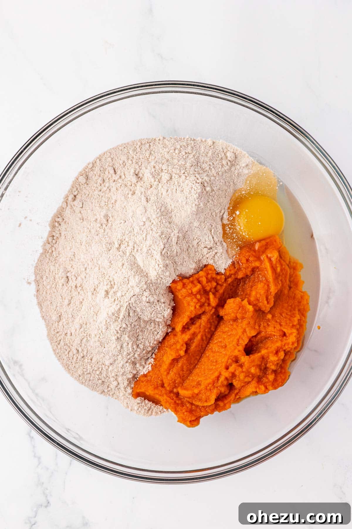 A mixing bowl containing an egg, pumpkin puree, and spice cake mix before being combined.