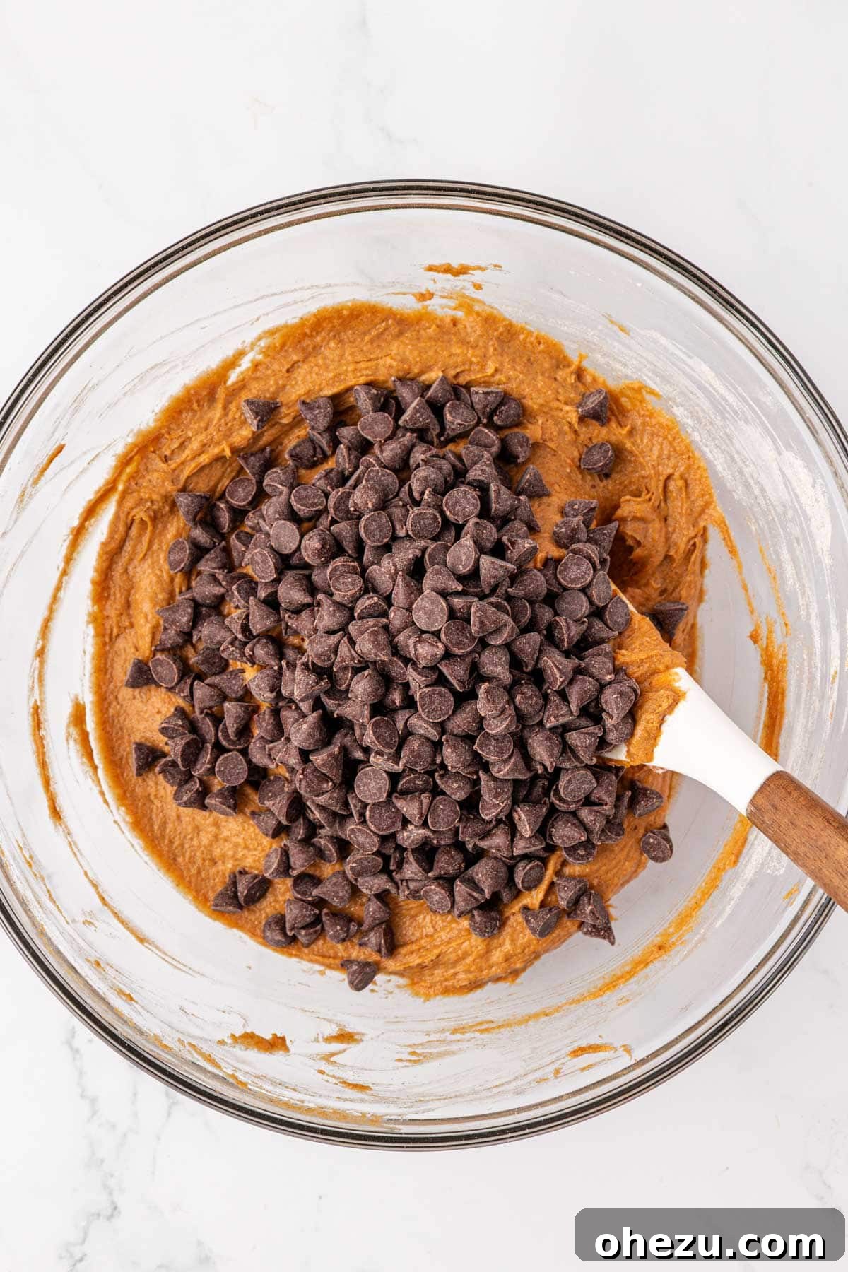 A hand gently adding semi-sweet chocolate chips into the prepared pumpkin cookie batter.