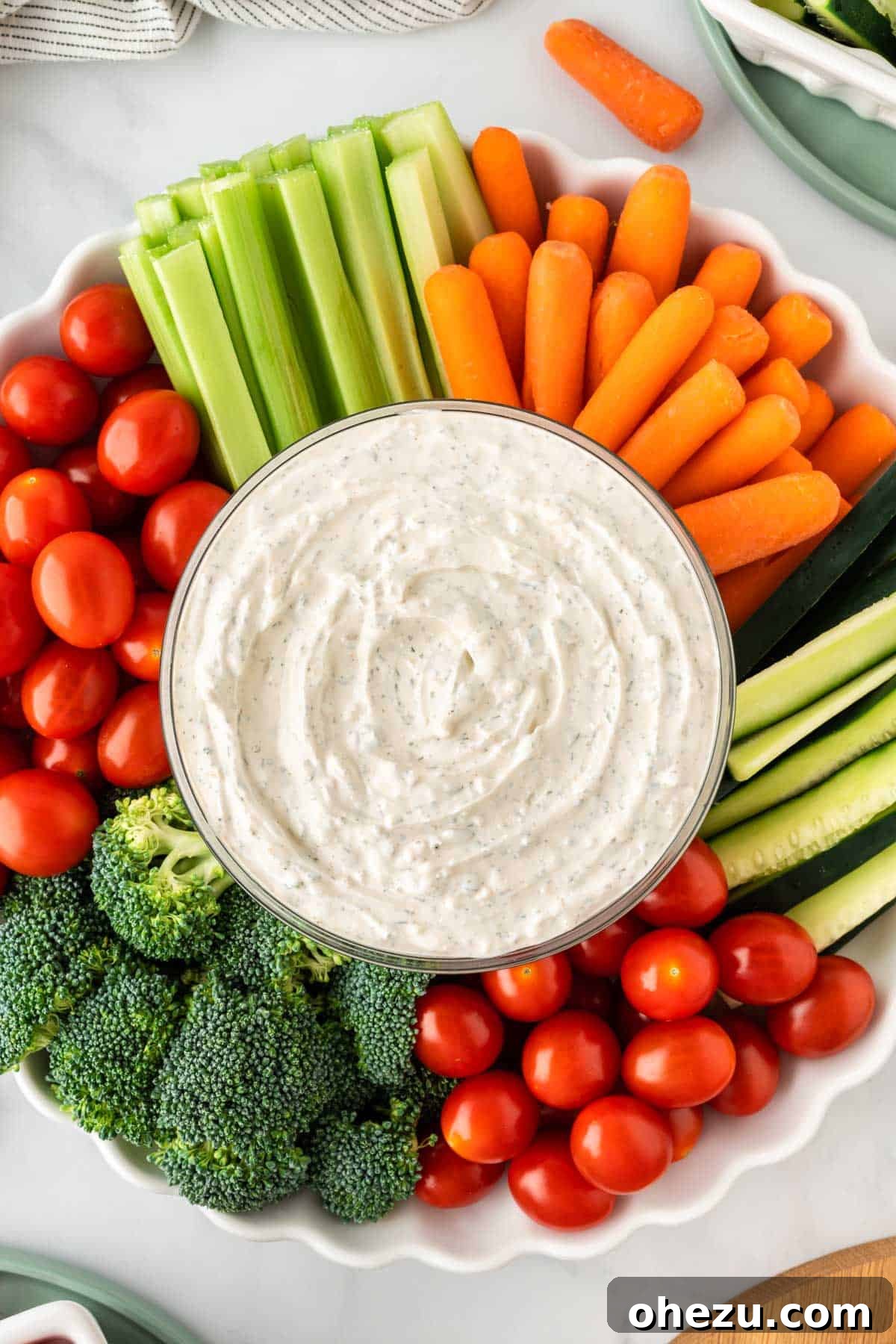 Garden Fresh Dip 2 A vibrant bowl of creamy veggie dip surrounded by an array of colorful, fresh raw vegetables including broccoli florets, bright red cherry tomatoes, crisp celery sticks, and sweet baby carrots.