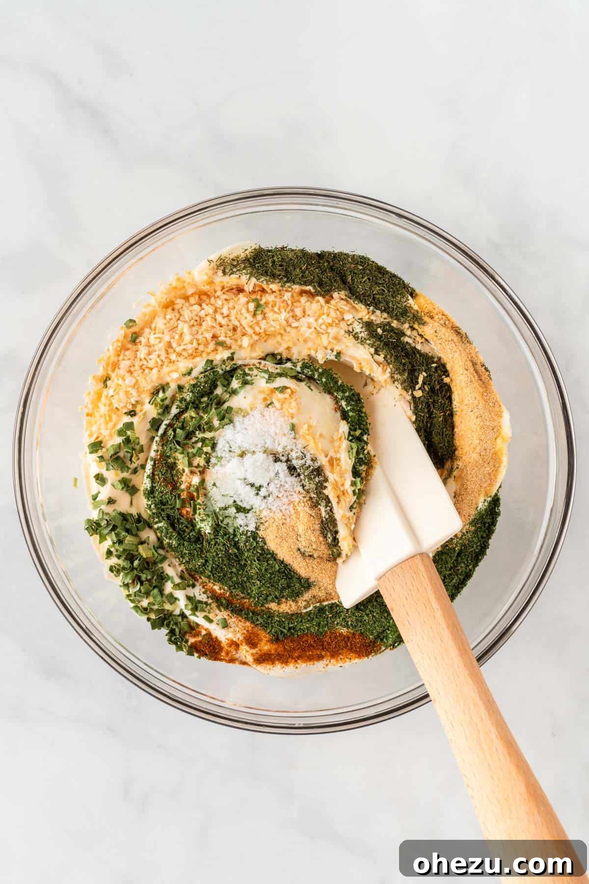 Garden Fresh Dip 6 A hand stirring the ingredients in a bowl with a spoon, thoroughly blending the sour cream, mayonnaise, and dried spices until smooth and evenly combined.