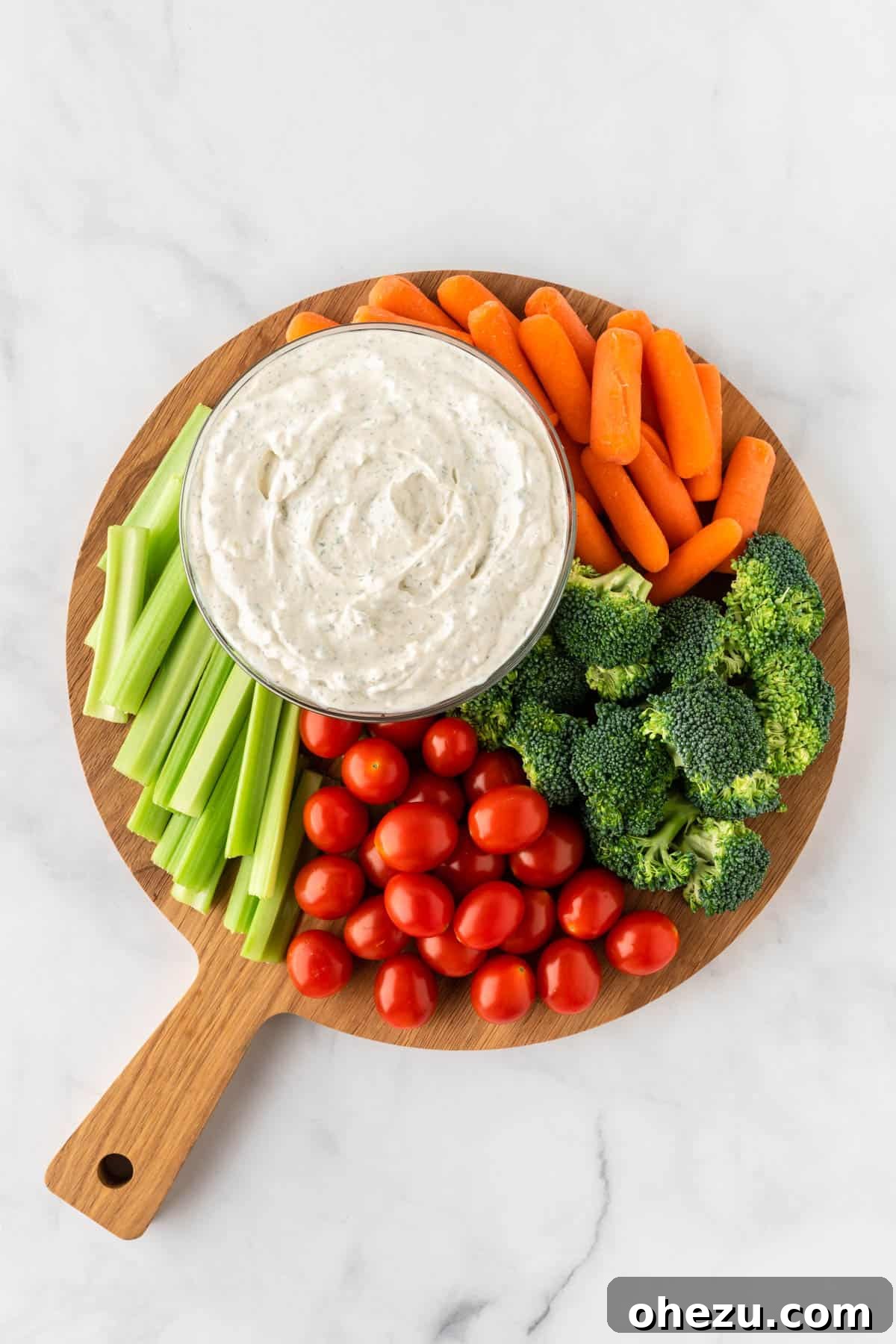 Garden Fresh Dip 8 A wooden cutting board laden with an assortment of freshly cut vegetables, including vibrant bell peppers, cucumbers, carrots, and celery, arranged around a bowl of homemade veggie dip.