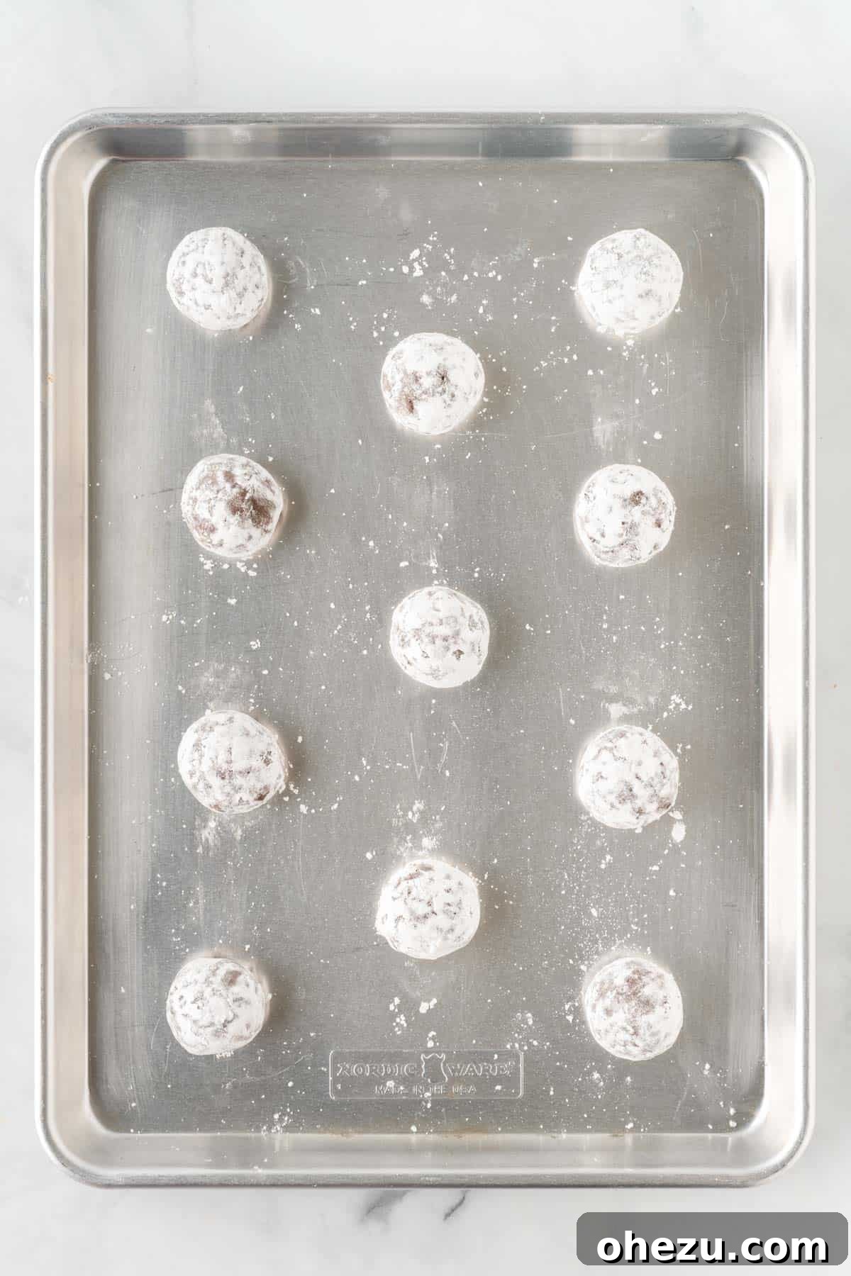 Cookie dough balls rolled in powdered sugar on a baking sheet