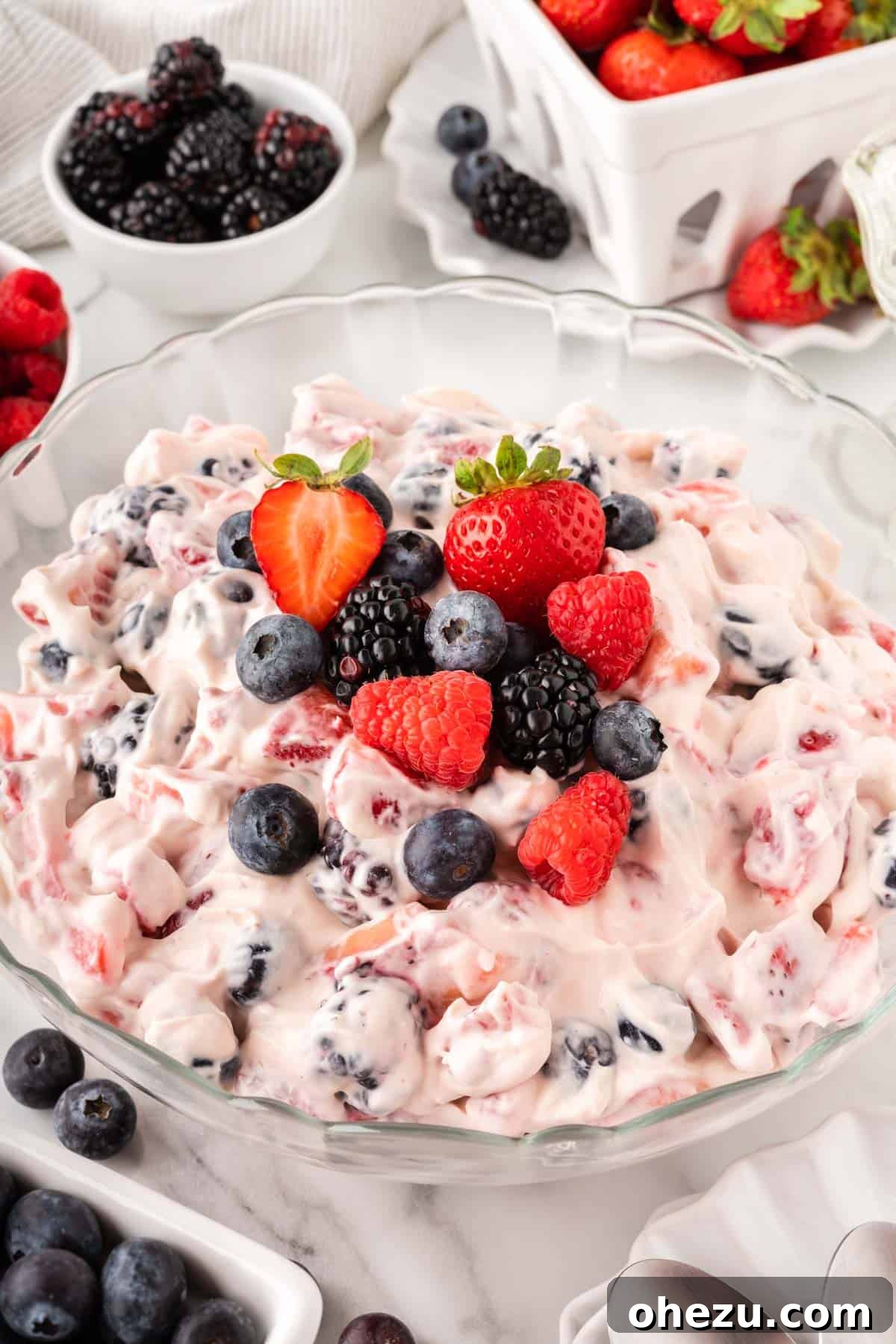A large bowl of creamy berry cheesecake salad topped with fresh strawberries, blueberries, blackberries, and raspberries, ready to be served.