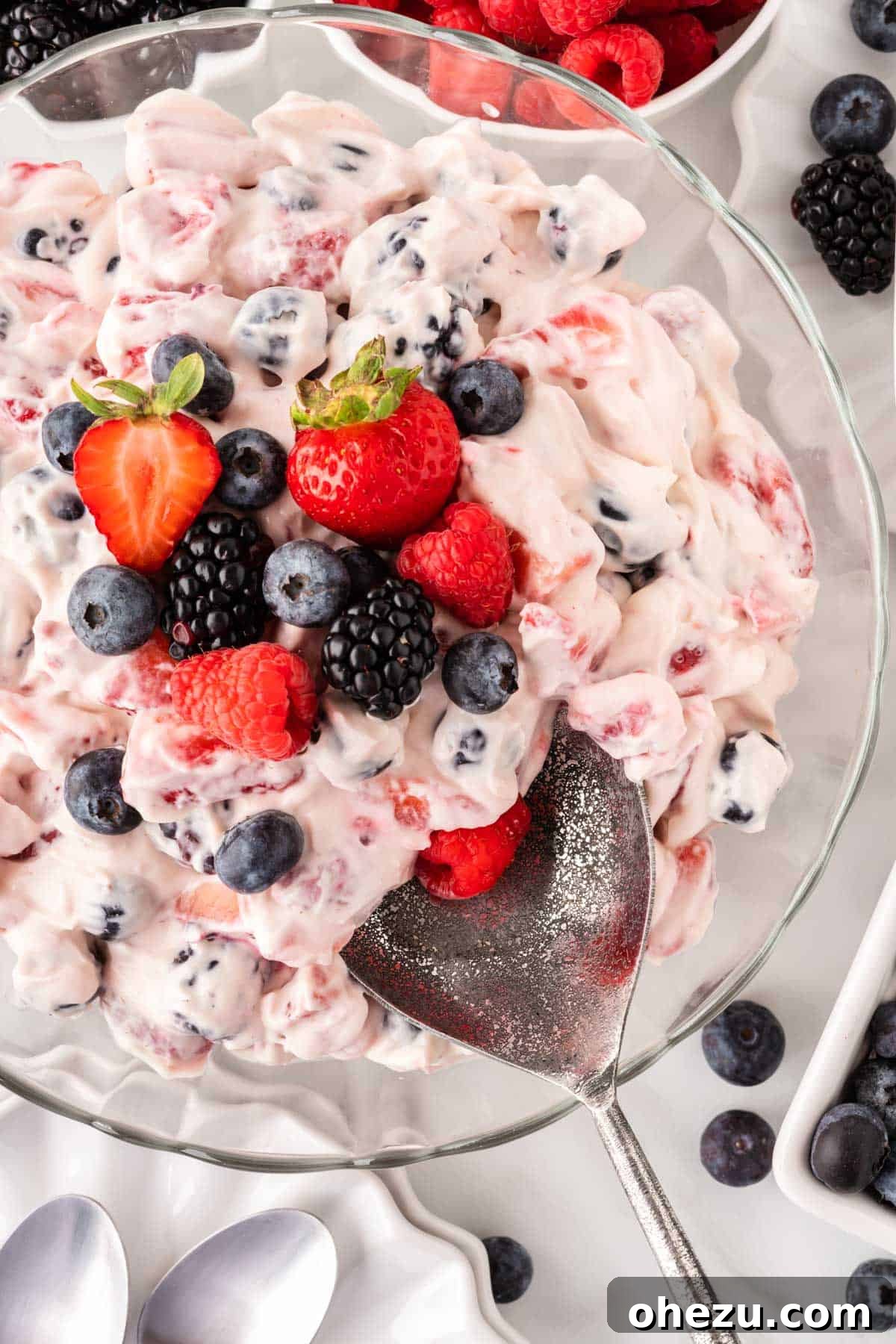 A serving spoon lifting a generous scoop of berry cheesecake salad from a bowl, highlighting the creamy texture and abundance of fruit.
