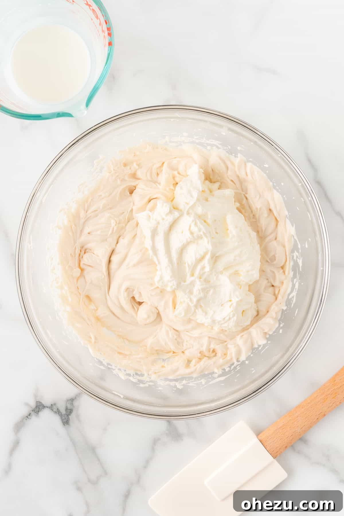 The process of adding the smooth cream cheese into the bowl of whipped cream, preparing for the final mix.