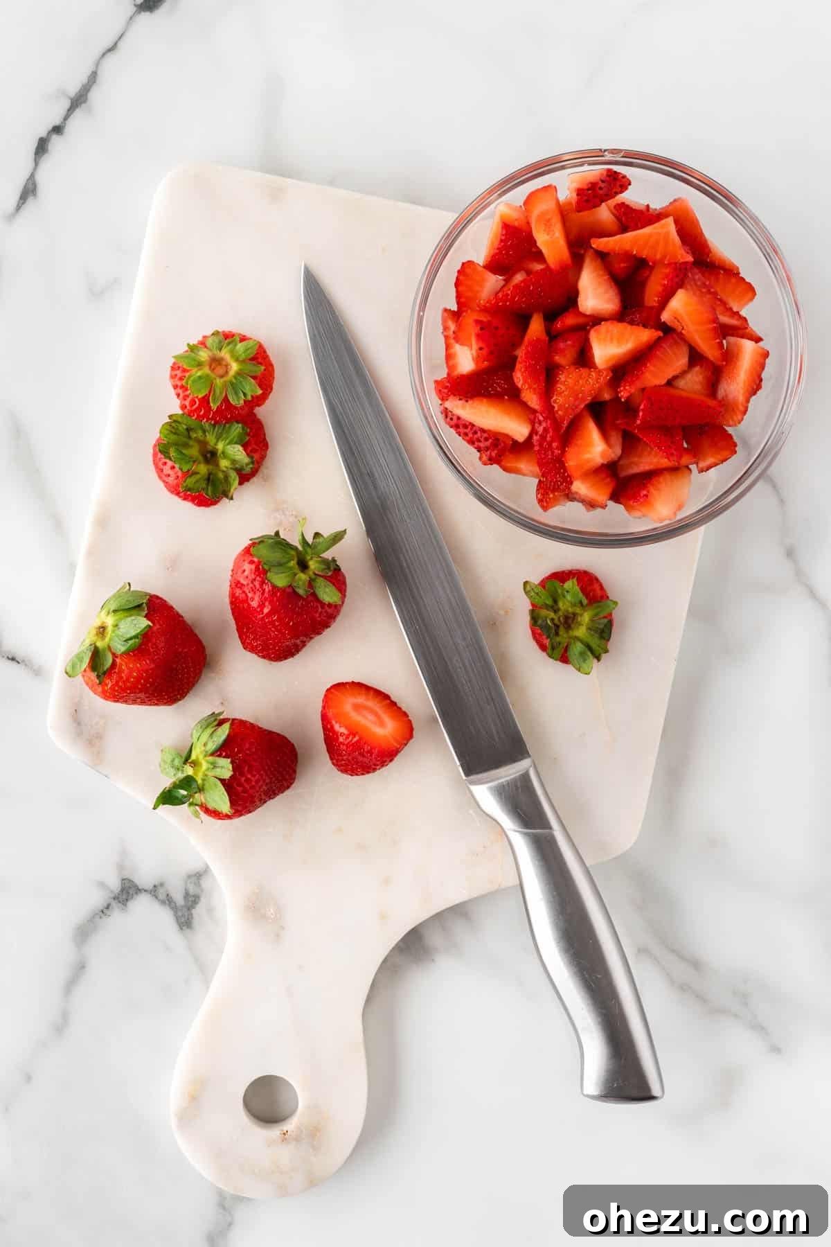 Hands carefully slicing fresh strawberries on a cutting board, preparing them for the cheesecake salad.