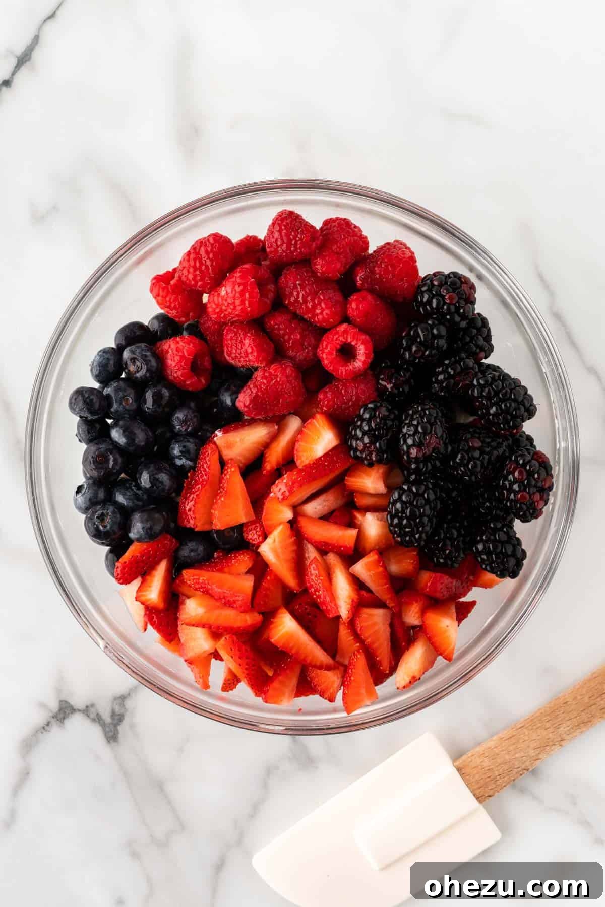 A colorful assortment of prepared strawberries, blackberries, raspberries, and blueberries in a clear bowl, ready to be added to the filling.