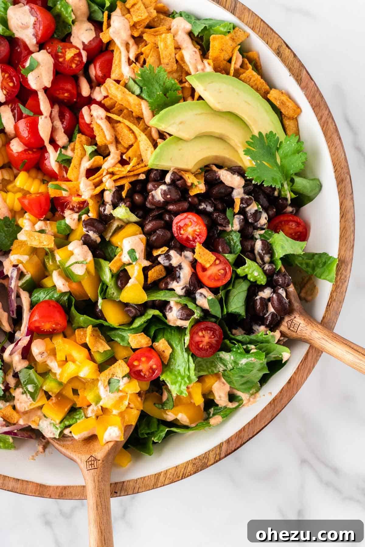 A top-down view of a colorful southwest salad with grilled corn, avocado, tomatoes, and a generous amount of chipotle ranch dressing.