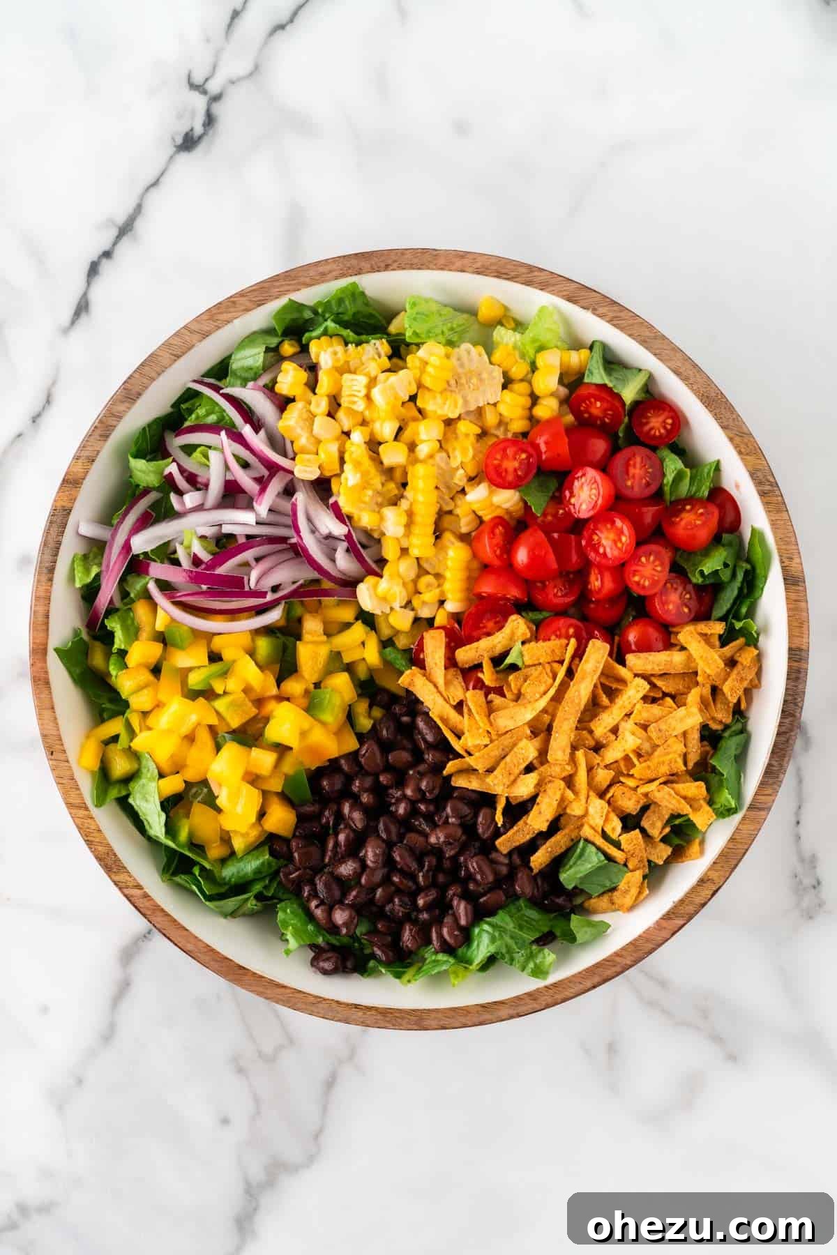Fiesta Fresh Salad 7 romaine lettuce topped with corn, bell pepper, cherry tomatoes, red onion, black beans, and tortilla strips, showcasing the colorful layers