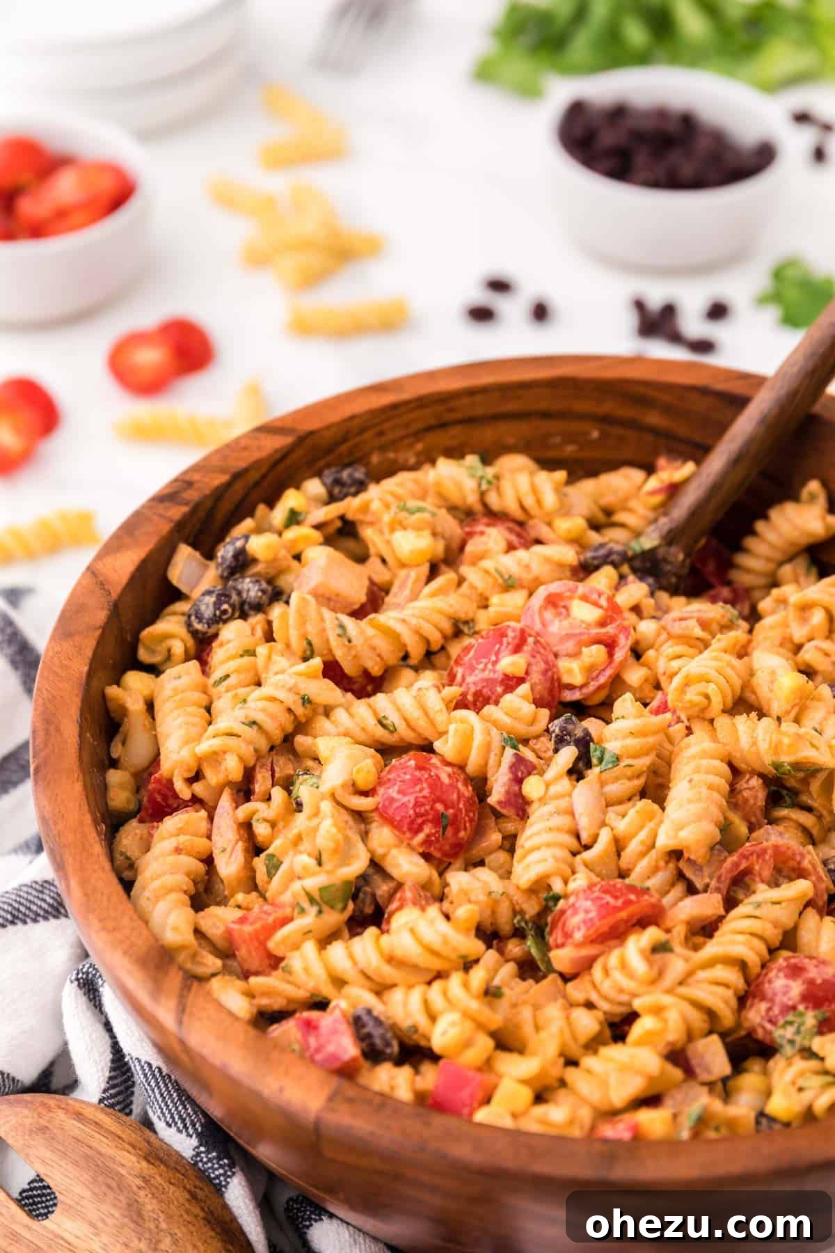 Zesty Fiesta Pasta Salad 2 A large brown serving bowl overflowing with a colorful southwest pasta salad, featuring rotini pasta, black beans, corn, red bell peppers, cherry tomatoes, and cilantro, all coated in a creamy dressing.
