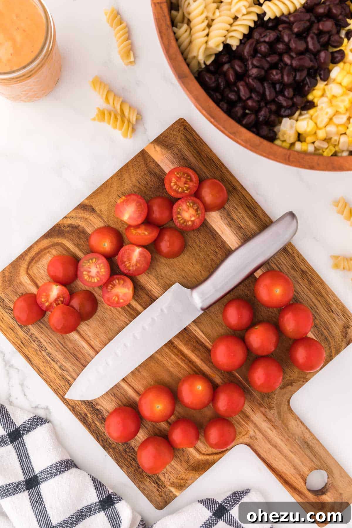 Zesty Fiesta Pasta Salad 6 Vibrant red cherry tomatoes, freshly halved, scattered on a wooden cutting board, prepared for inclusion in the salad.