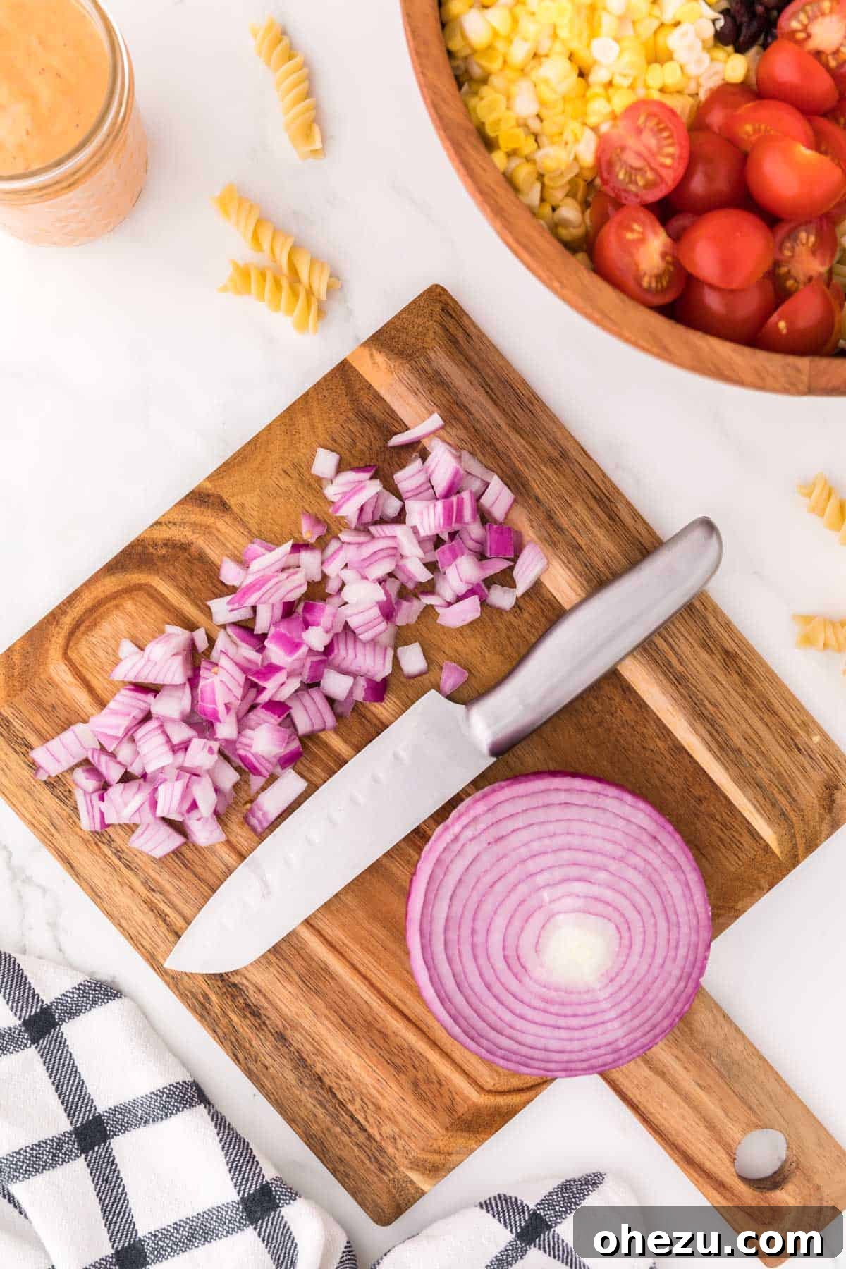 Zesty Fiesta Pasta Salad 7 Finely chopped red onions scattered on a wooden cutting board, showing their vibrant purple hue.