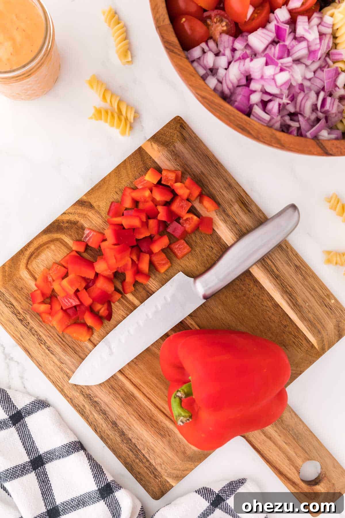 Zesty Fiesta Pasta Salad 8 Diced red bell pepper pieces laid out on a wooden cutting board, showcasing their bright color and uniform cut.