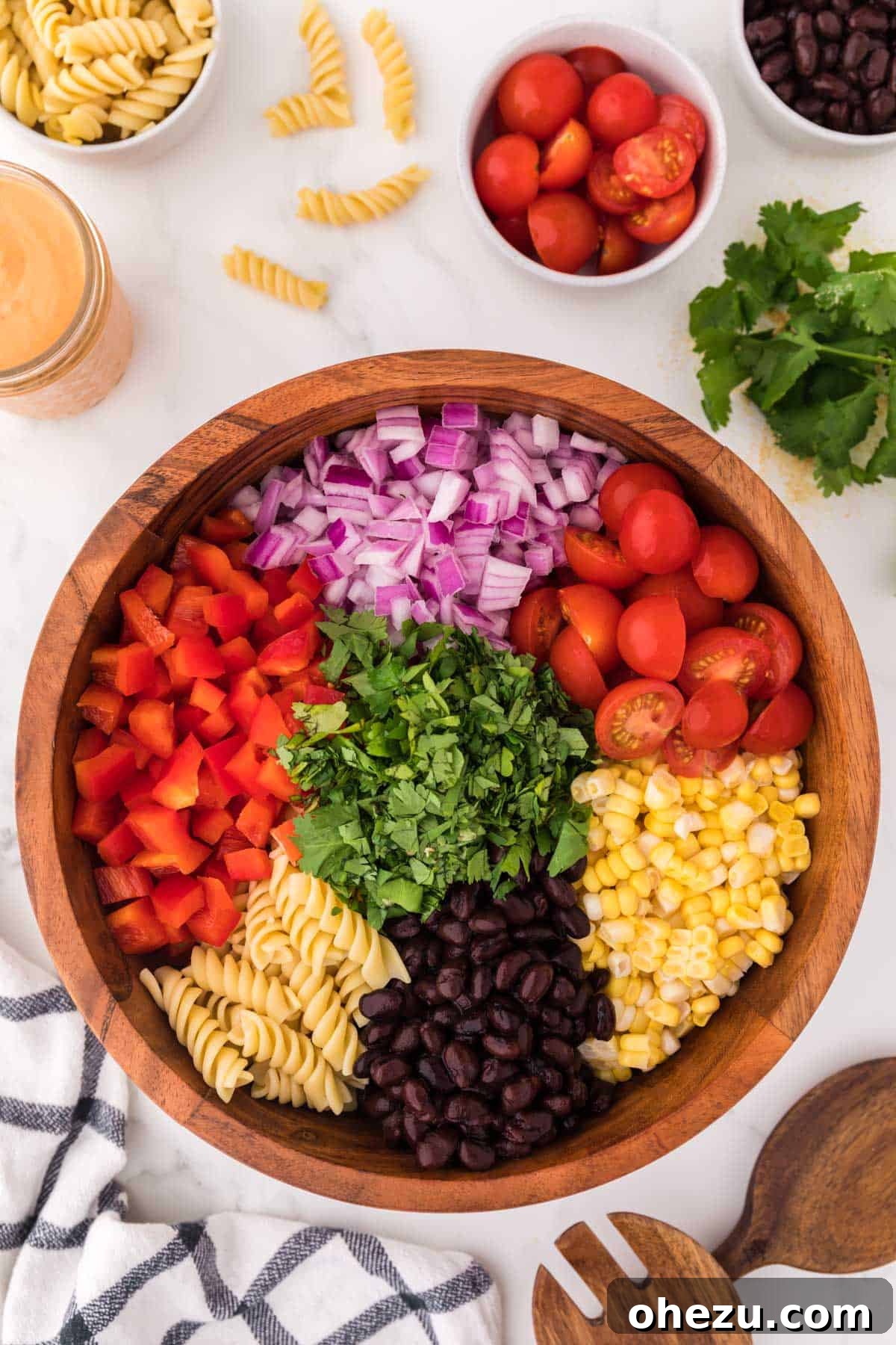 Zesty Fiesta Pasta Salad 9 A large mixing bowl filled with unmixed southwest pasta salad ingredients, including cooked rotini, black beans, corn, bell pepper, onion, tomatoes, and cilantro, ready for dressing.