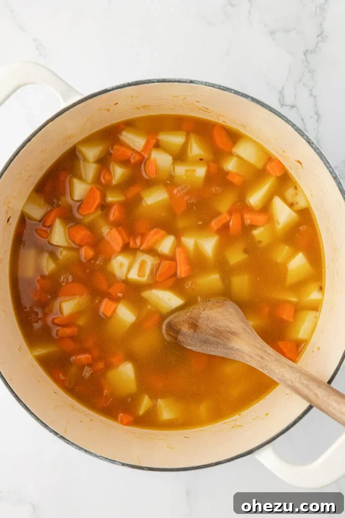 A close-up shot of a spoon gently stirring the tender vegetables into the broth, ensuring all components are well combined and cooked evenly.