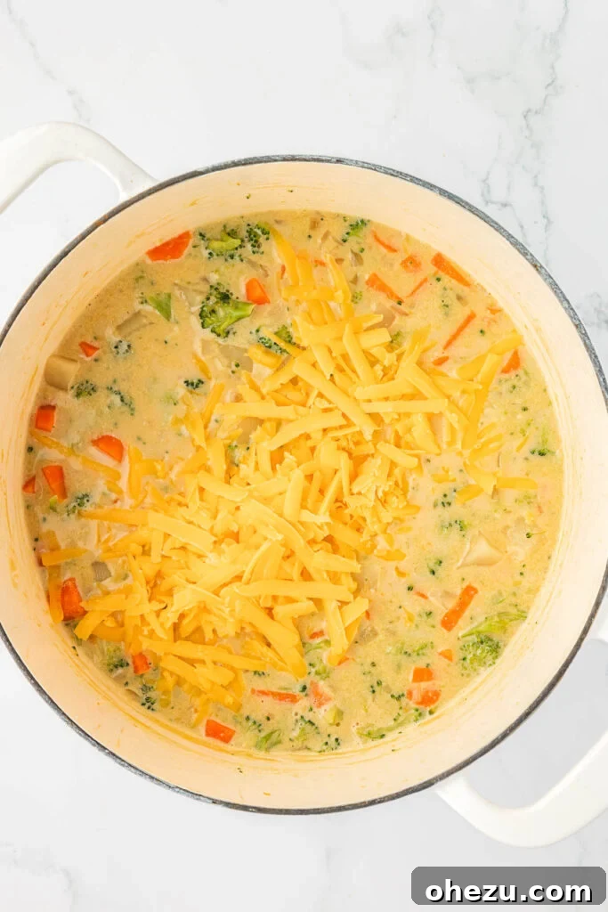 A generous handful of freshly grated sharp cheddar cheese being added to the hot, creamy vegetable soup, ready to melt into a luscious, rich consistency.