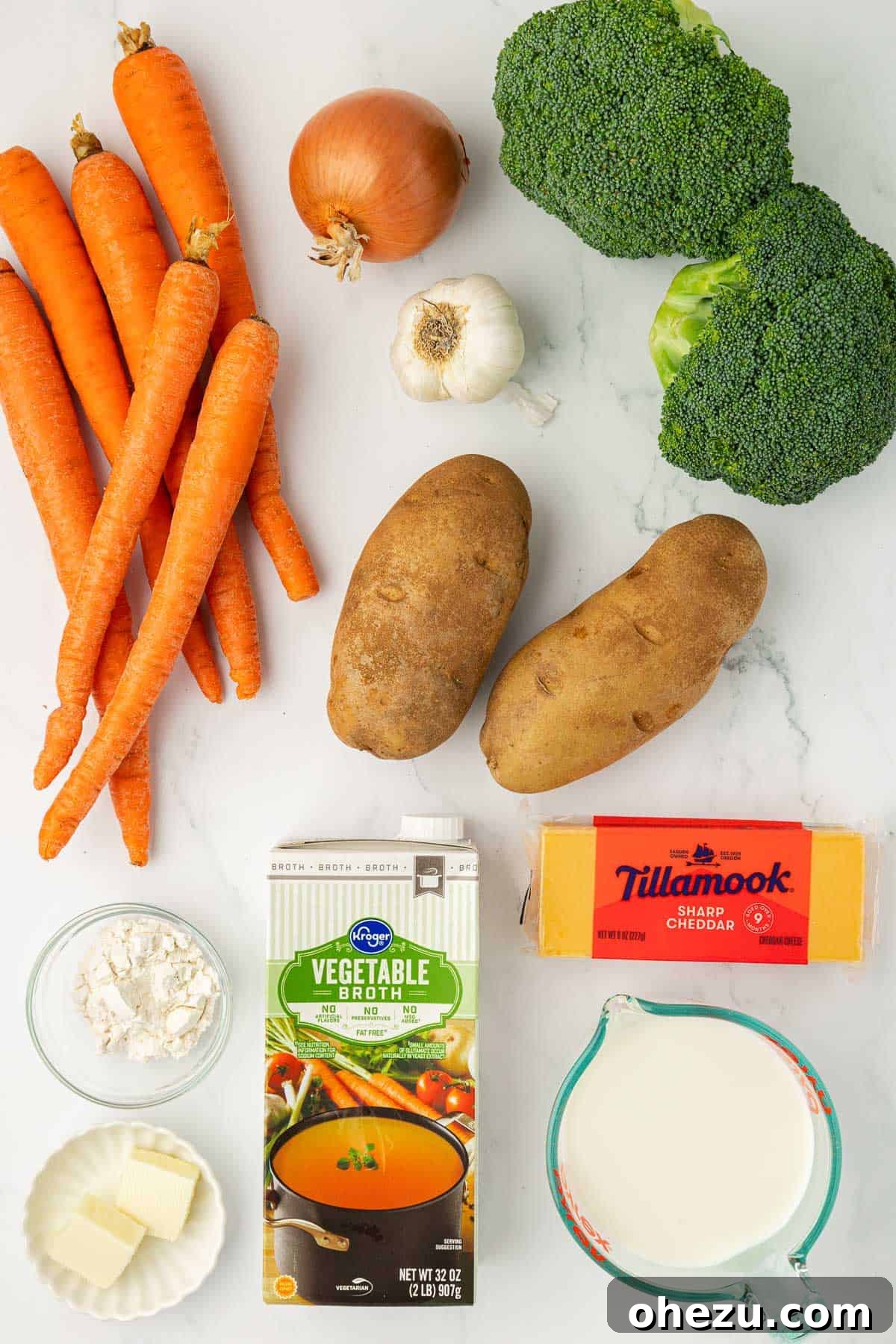 A beautiful flat lay photo showcasing all the fresh, high-quality ingredients laid out for making the creamy vegetable soup, including brightly colored carrots, a yellow onion, pungent garlic, crisp broccoli florets, hearty russet potatoes, rich butter, all-purpose flour, vegetable broth, creamy sharp cheddar cheese, and wholesome milk.