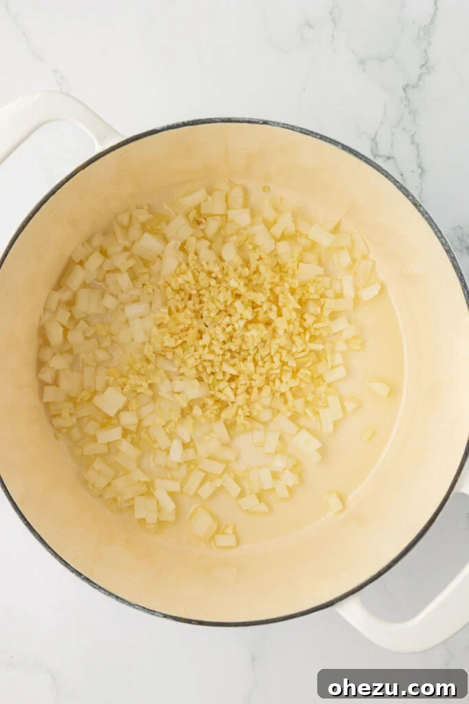 A close-up view of minced garlic and diced onion gently sautéing in shimmering melted butter within a sturdy Dutch oven, filling the kitchen with a wonderful aroma.