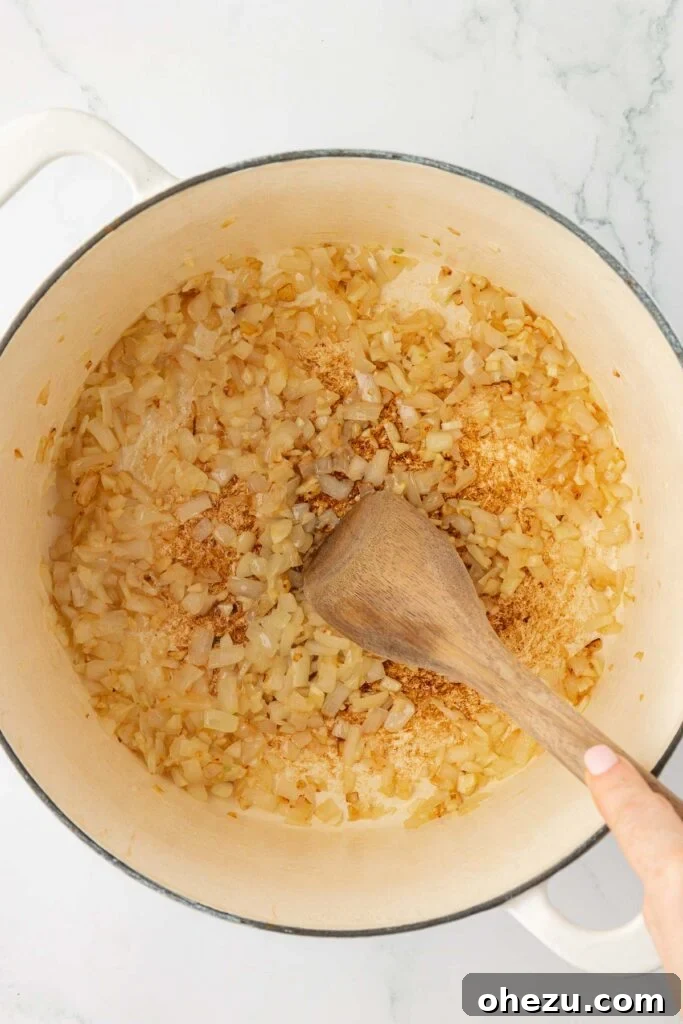 A wooden spoon delicately stirring the softened and translucent garlic and onion mixture in a Dutch oven, indicating they have cooked down perfectly and are ready for the next ingredient.