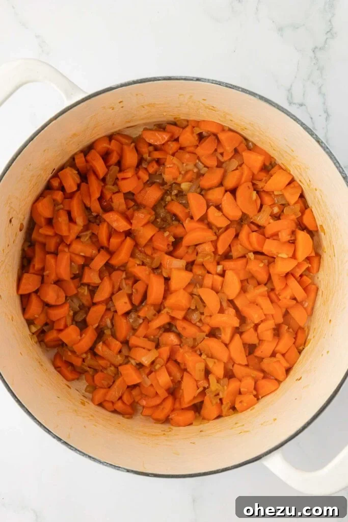 The harmonious medley of cooked-down carrots, onions, and garlic in the Dutch oven, glistening and fragrant, signifying a well-developed and deeply flavored foundation for the soup.