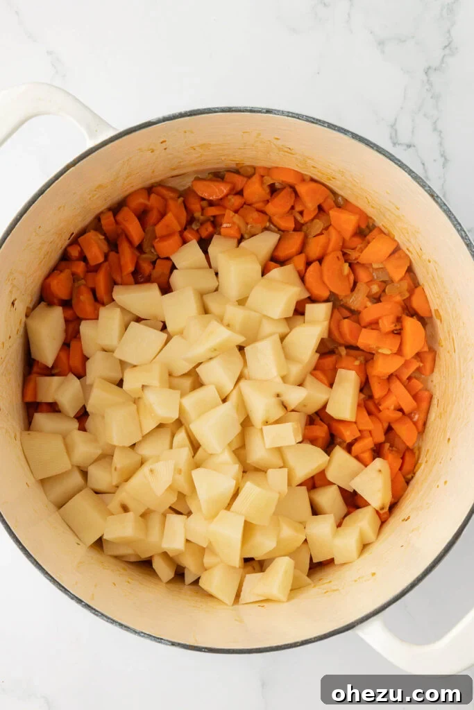 Finely diced potatoes being carefully added to the Dutch oven, joining the cooked carrots, onions, and garlic for the simmering process.
