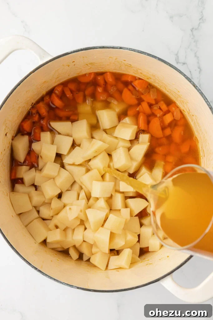 A rich vegetable broth being poured over the potatoes and carrots in the Dutch oven, setting the stage for the vegetables to soften and flavors to meld.