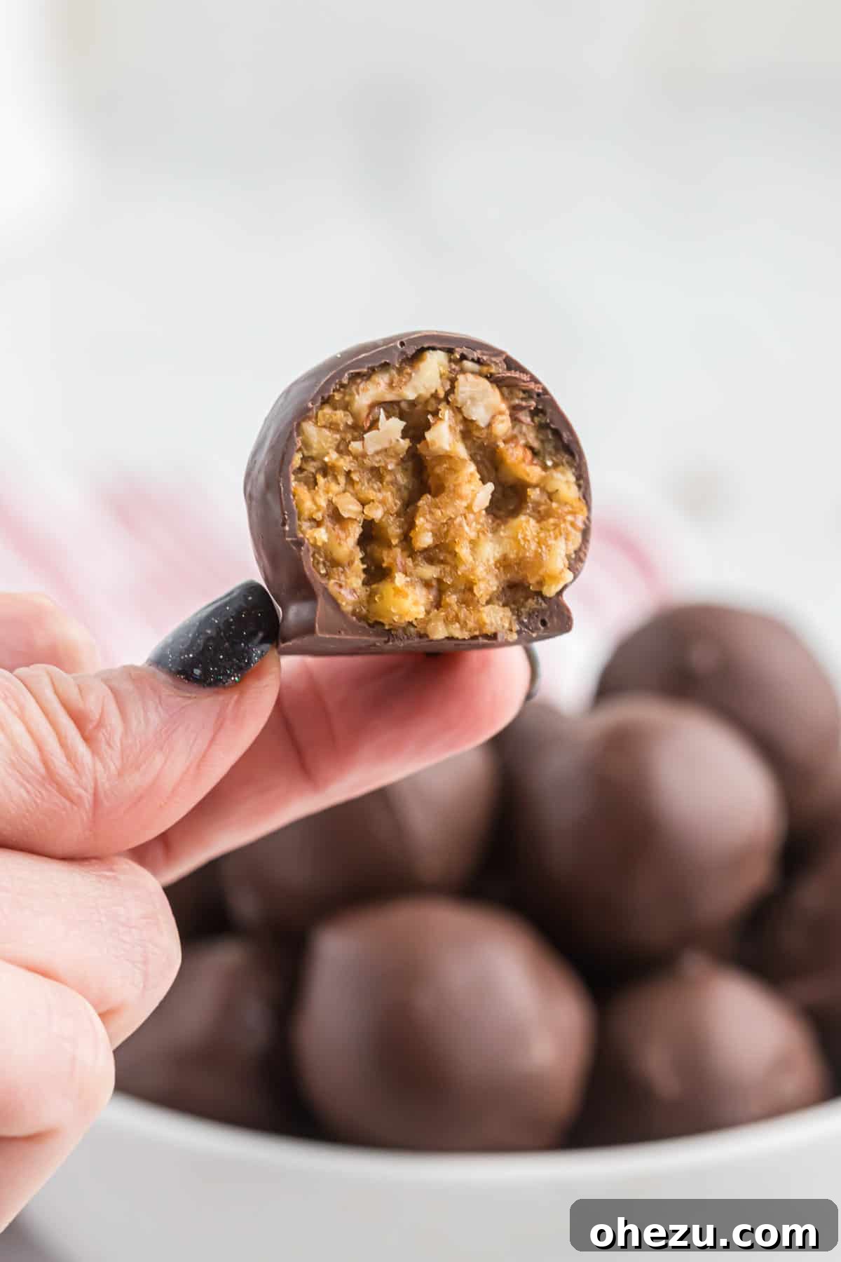 Pecan Pie Truffles 11 A hand holding a pecan pie ball with a bite taken out, emphasizing its delicious texture and chocolate coating.