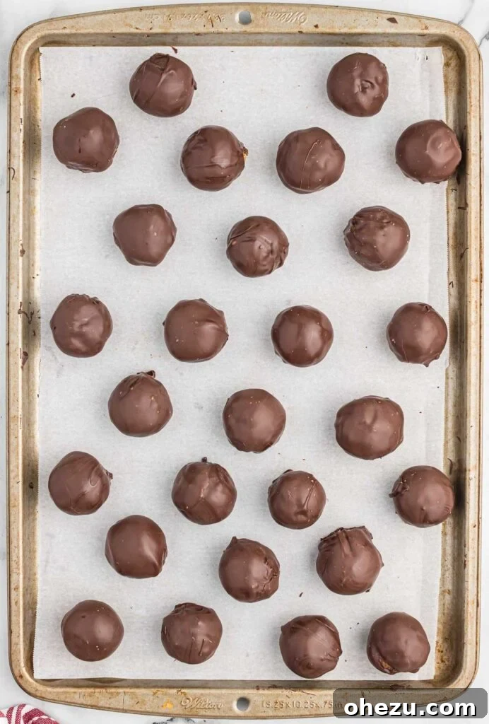 Pecan Pie Truffles 9 Chocolate-covered pecan balls cooling and setting on a parchment-lined baking sheet.