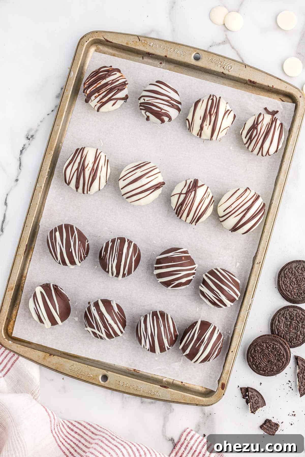 An array of oreo balls, some dark chocolate-dipped and drizzled with white, others white chocolate-dipped and drizzled with dark, on a baking sheet.