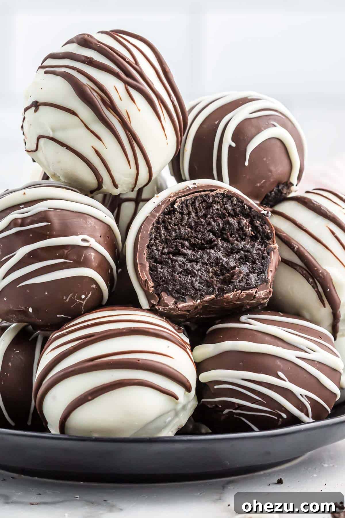 A selection of beautifully decorated oreo balls on a white serving plate, showcasing different chocolate coatings and drizzles.