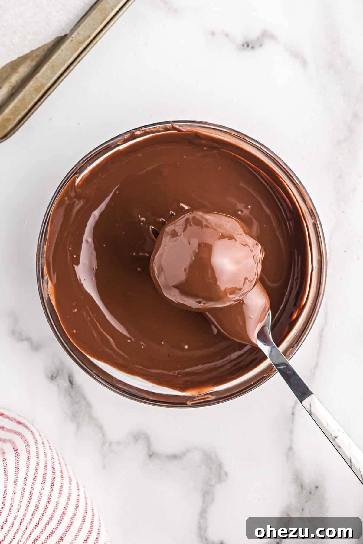 A freshly dipped Oreo ball, glistening with a smooth coat of dark chocolate, resting on a fork.